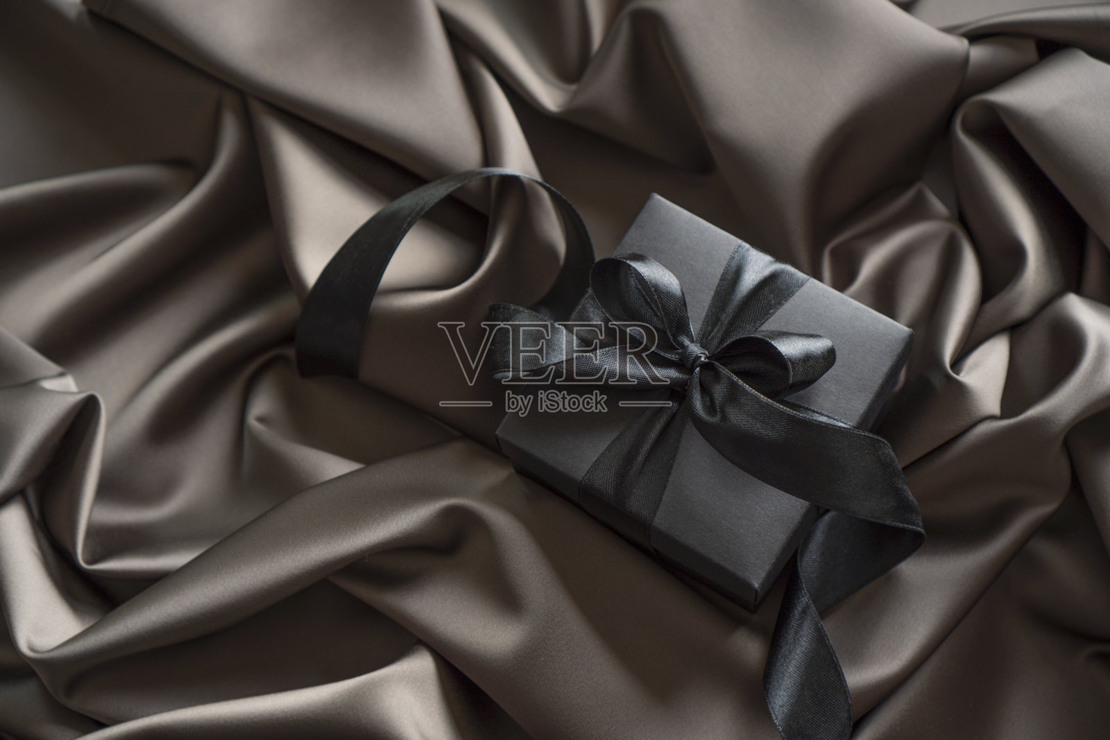 黑色礼品盒与黑色蝴蝶结丝带在缎子床上。照片摄影图片