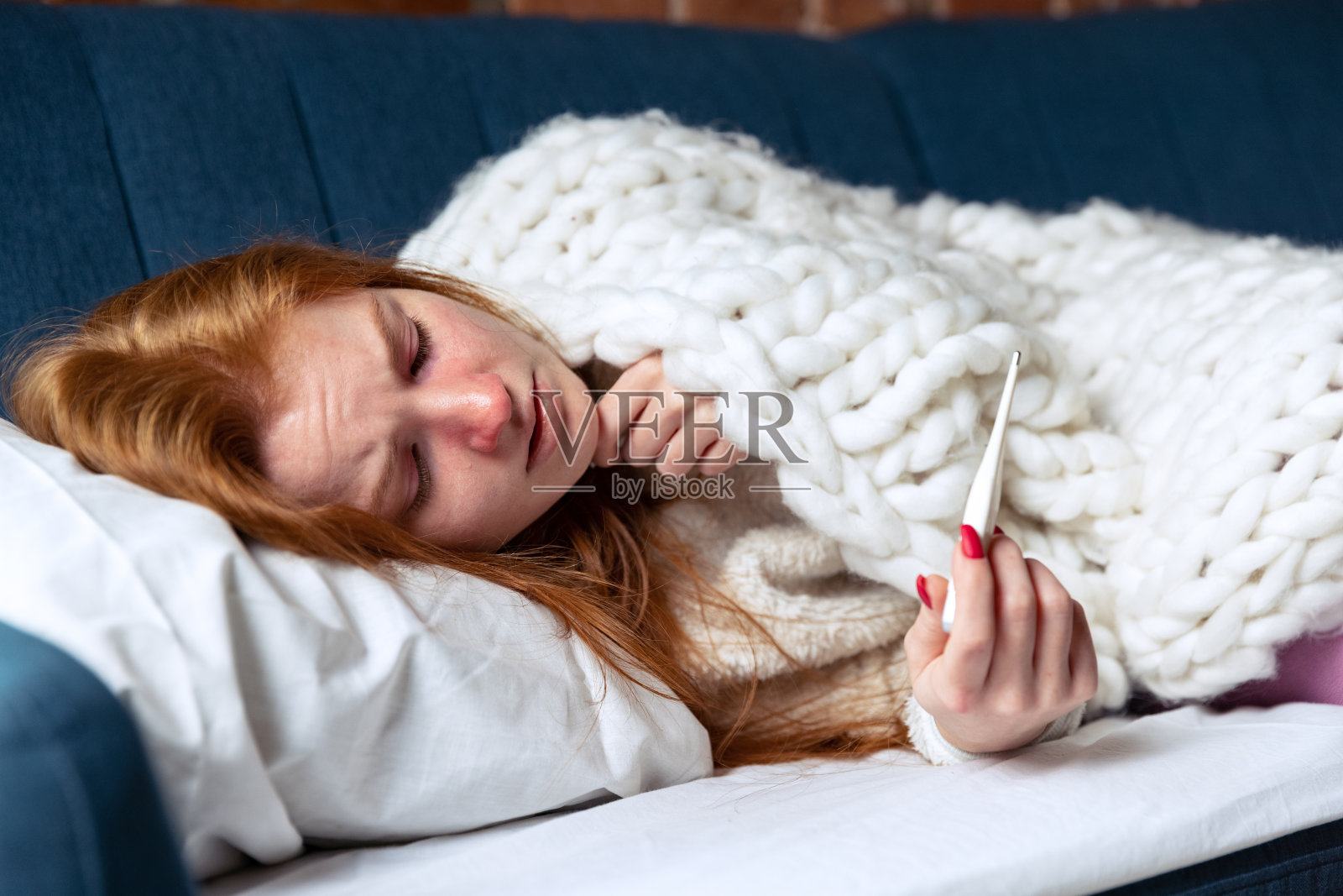 年轻女孩的裁剪肖像躺在沙发上，测量温度。感觉病了。照片摄影图片