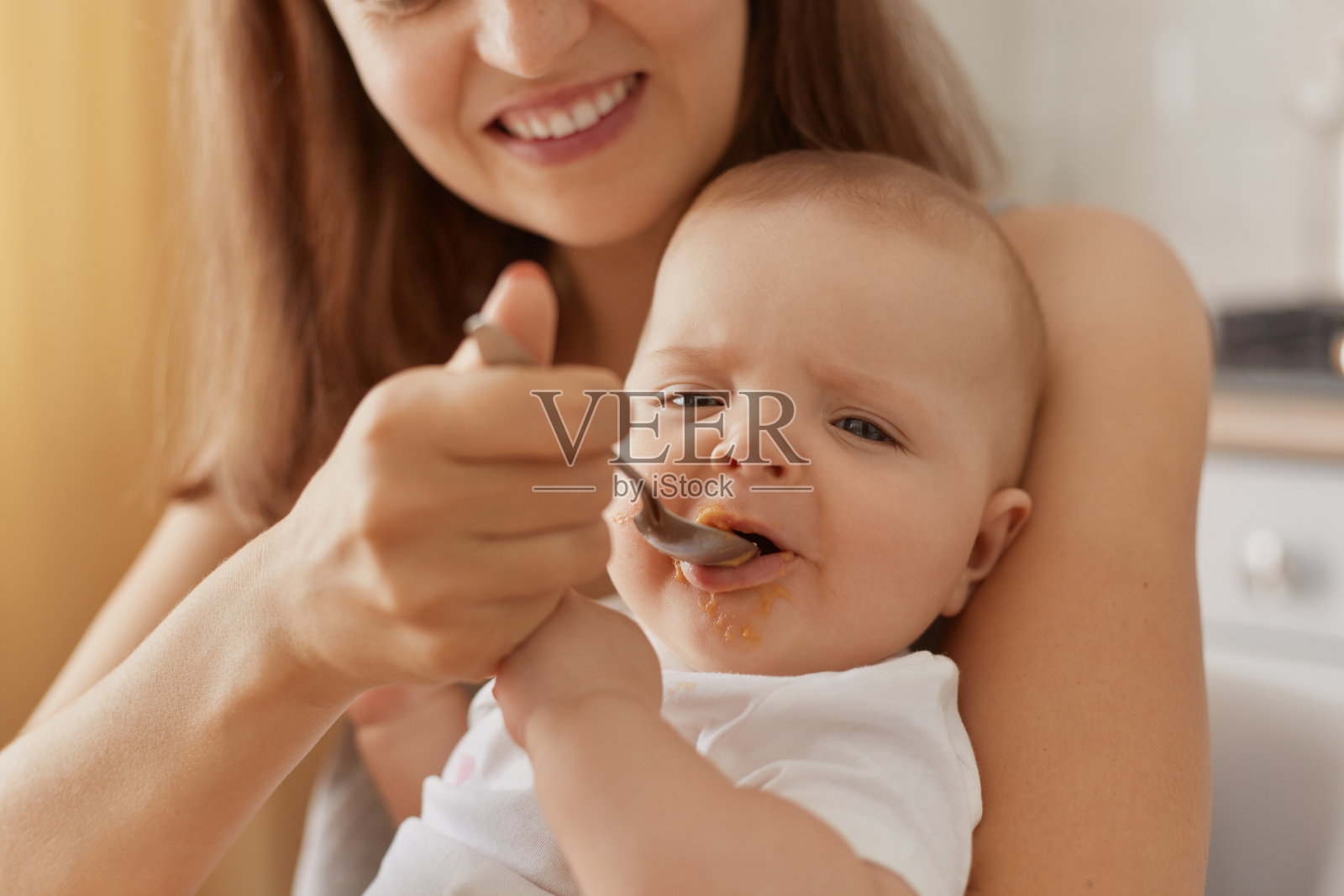 微笑快乐的妈妈在家里用塑料勺给可爱的小宝贝吃蔬菜或水果泥，给孩子补充营养，给孩子健康的食物。照片摄影图片