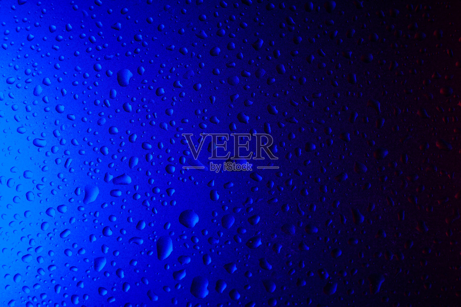 蓝色霓虹灯下玻璃上的水滴。照片摄影图片