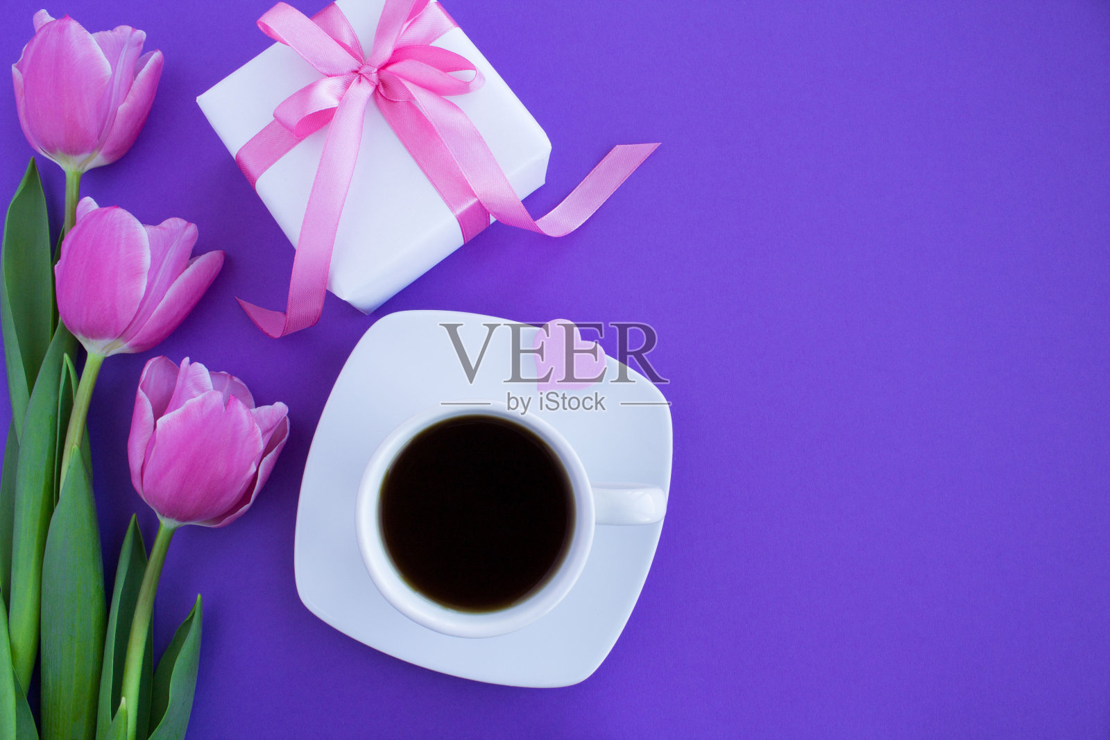 白色杯子里的黑咖啡，紫色背景上的礼品盒和粉色郁金香。前视图。特写镜头。照片摄影图片