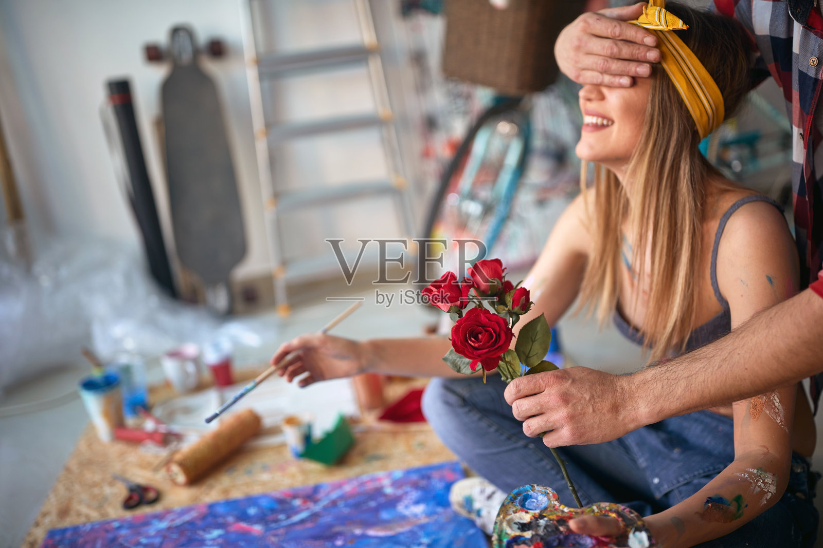 一个性感和有吸引力的女艺术家坐在她的工作室的地板上，而被她的男朋友与鲜花惊讶。艺术、绘画、工作室照片摄影图片