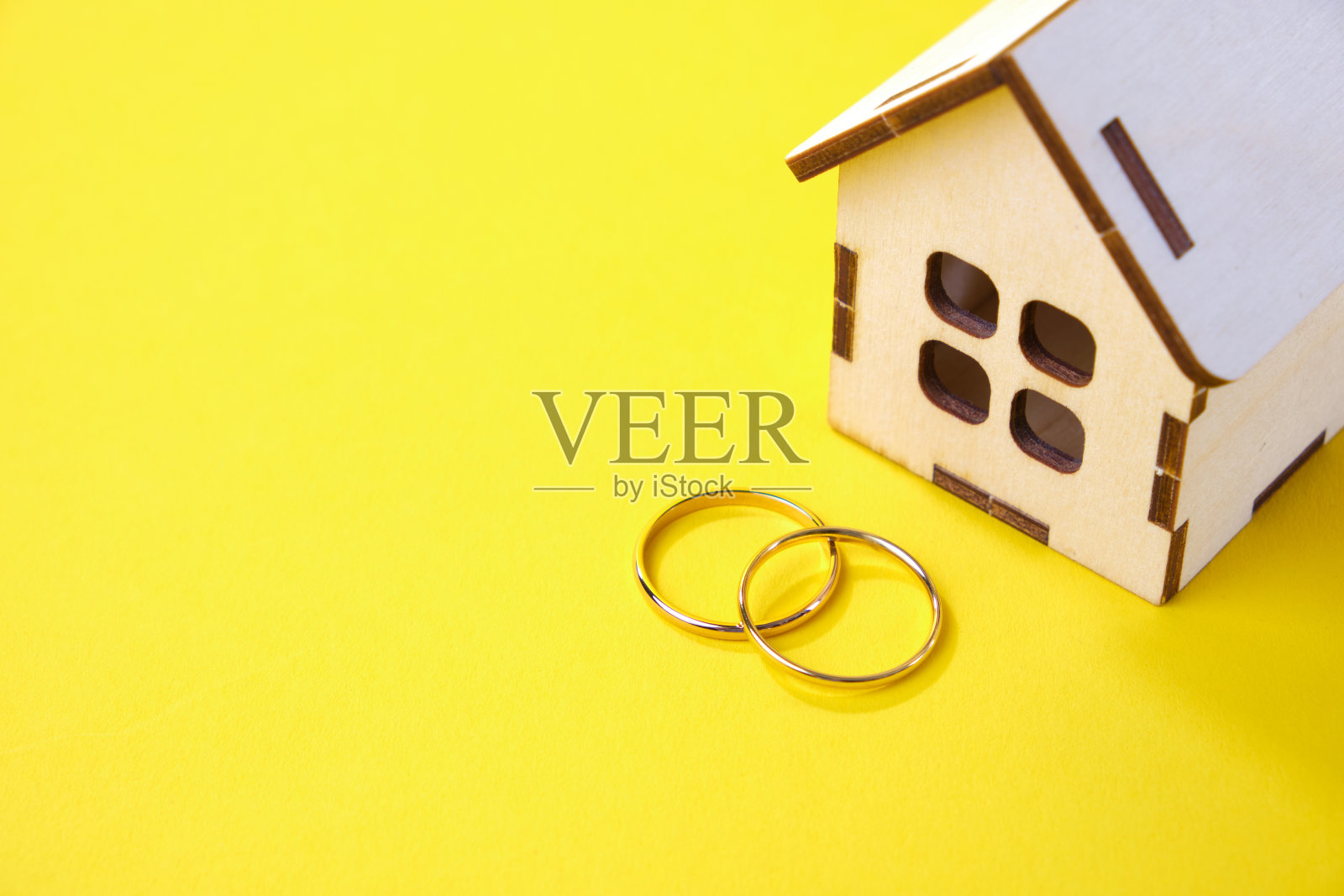 黄色背景上有结婚戒指的木制玩具屋。把一个年轻的家庭搬到新家的概念照片摄影图片