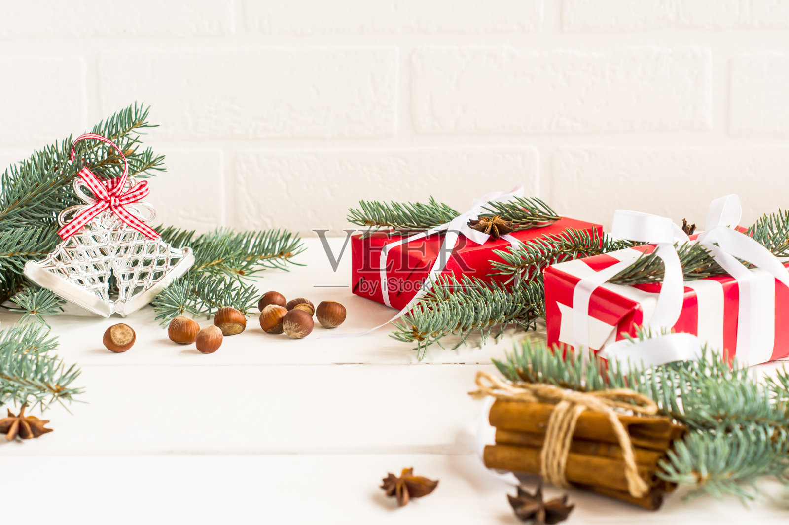 白色木制背景上的新年节日构图。礼品盒、装饰过的云杉树枝、坚果和肉桂棒放在桌上。照片摄影图片