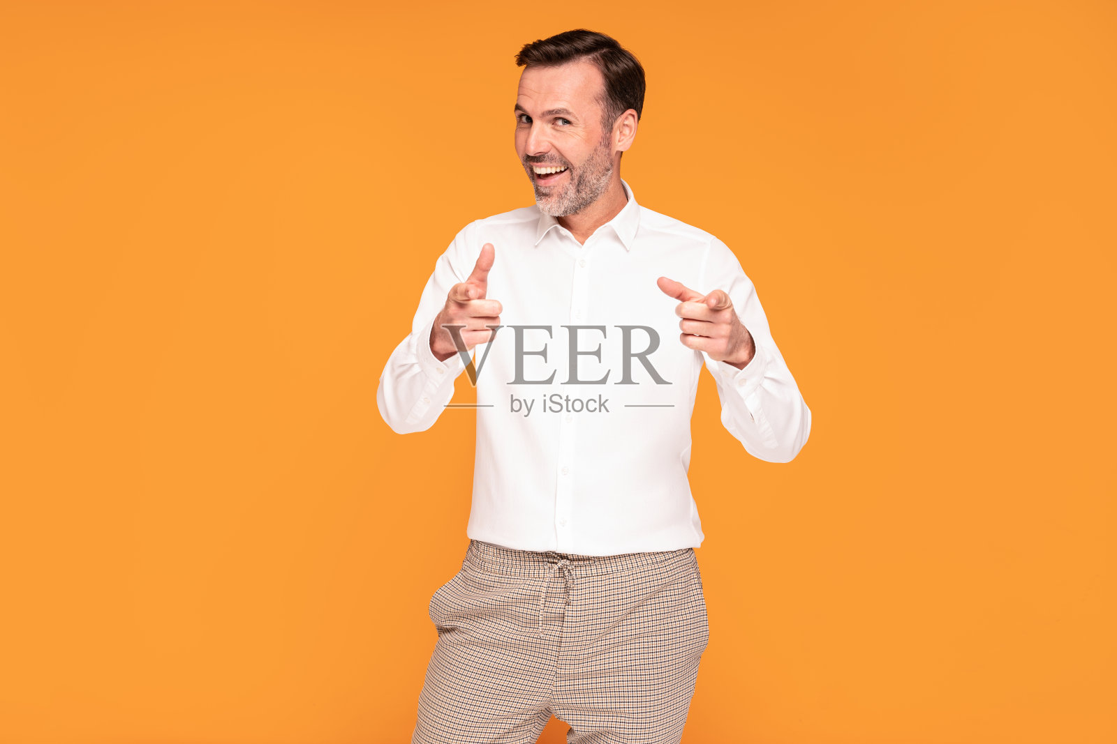 英俊快乐的男人微笑着看着镜头，用手指指着你，孤立在黄色的摄影棚背景上。照片摄影图片