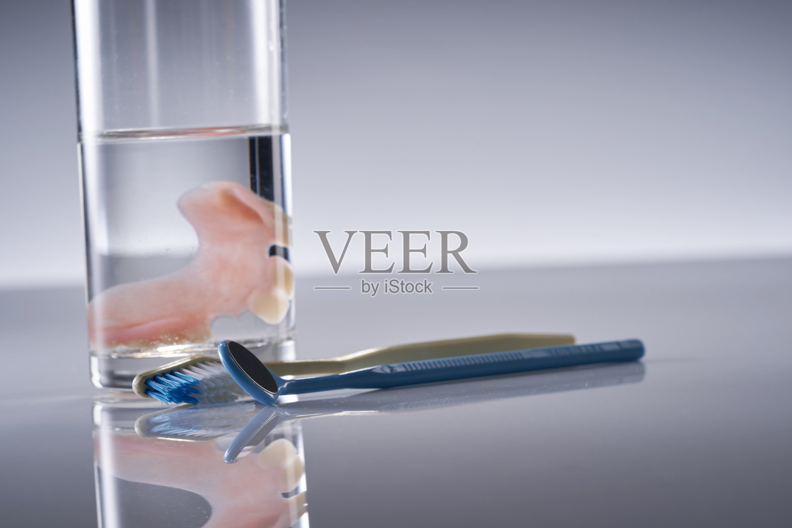 假牙放在装有牙刷和镜子的水里。假牙齿保健。照片摄影图片