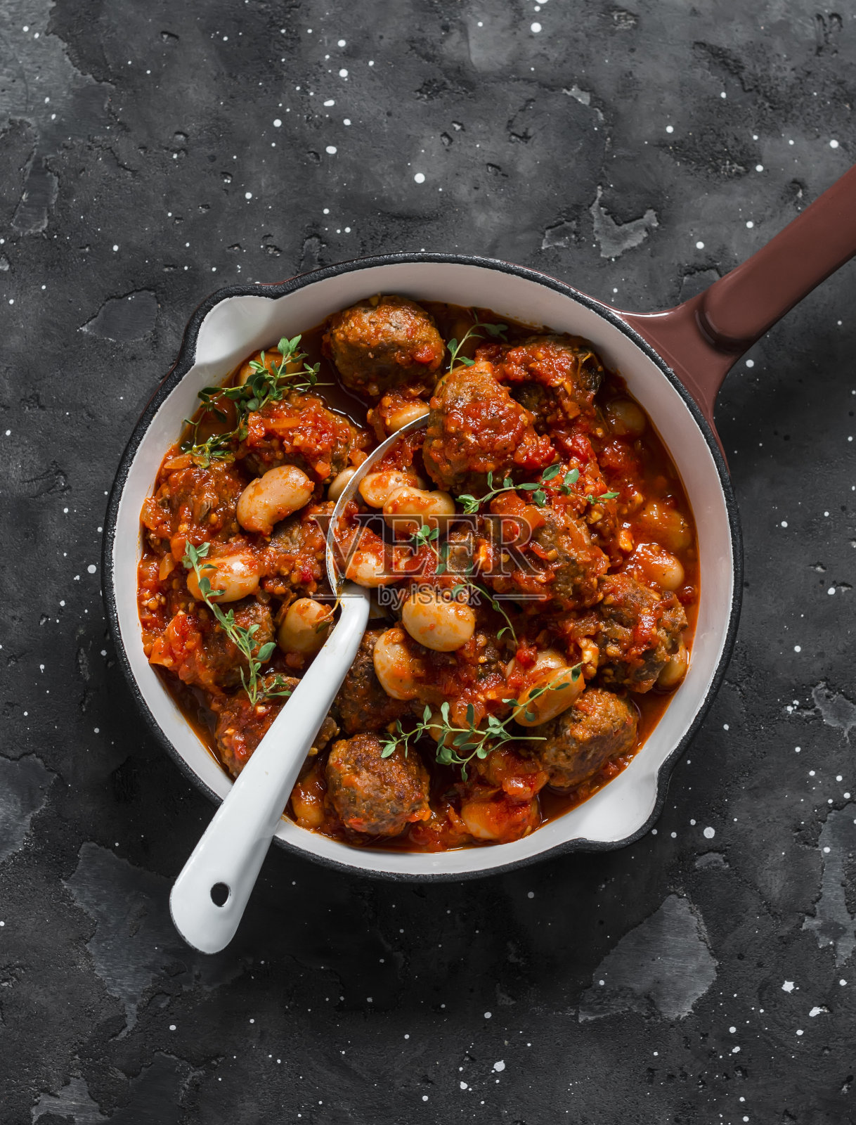 肉丸和豆子用番茄酱和香料炖在煎锅里，背景为黑色，俯视图照片摄影图片