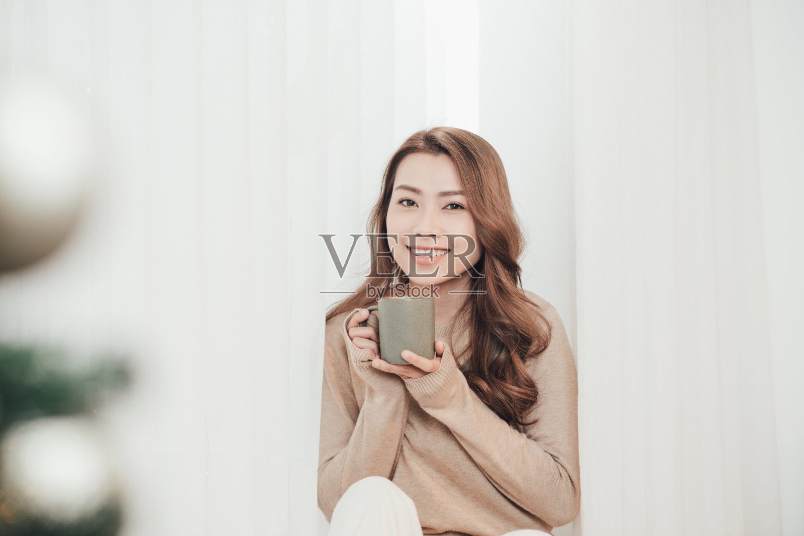 漂亮的年轻女士拿着杯子坐在家里的窗台上照片摄影图片