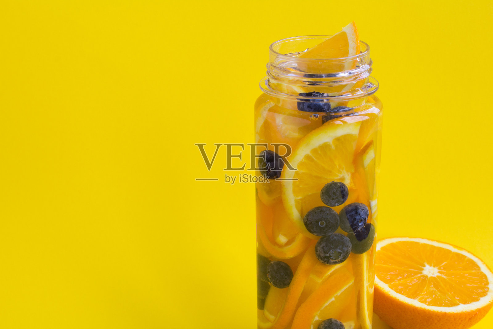 在黄色背景的瓶子里加入橙和蓝莓的排毒水。副本的空间。照片摄影图片