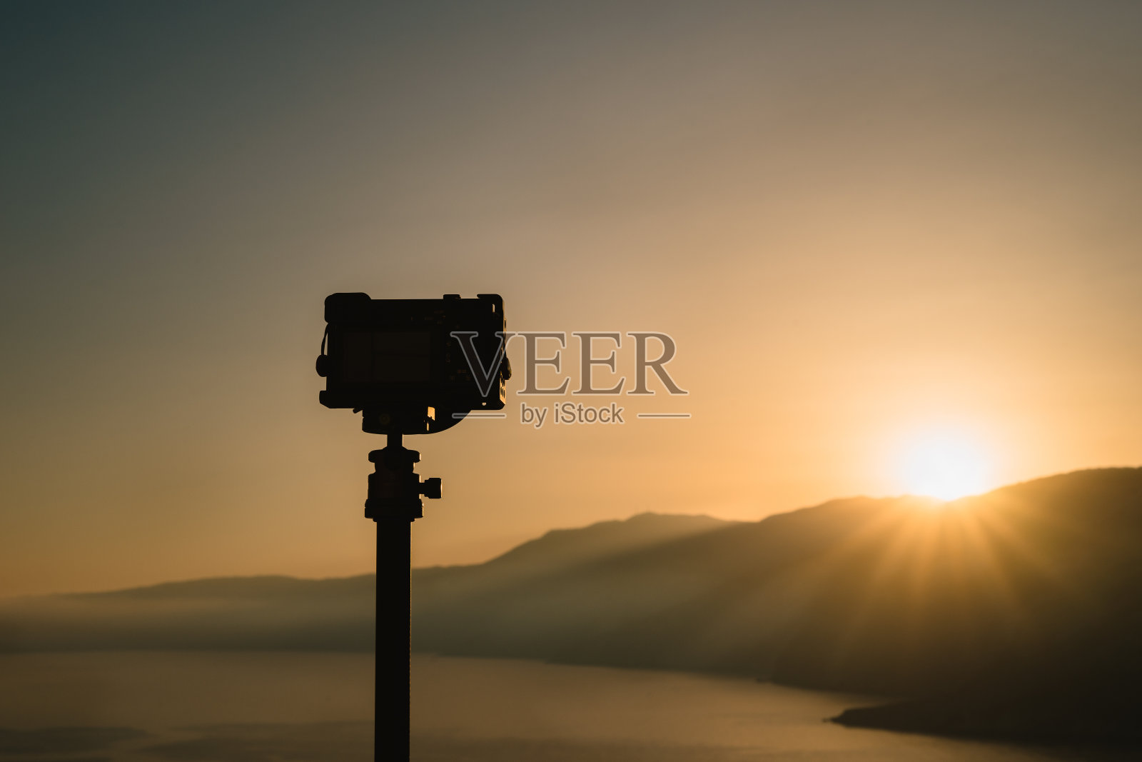 三脚架上的相机摄影师拍摄惊人的日出在山峰和平静的海湾。照片摄影图片