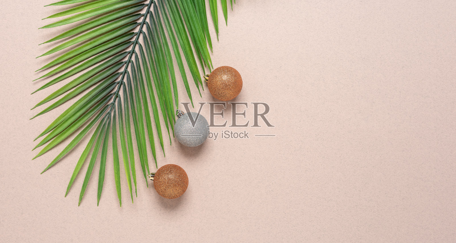 米色牛皮纸上的人造棕榈树枝和圣诞球。圣诞组成。俯视图，平铺，宽构图照片摄影图片
