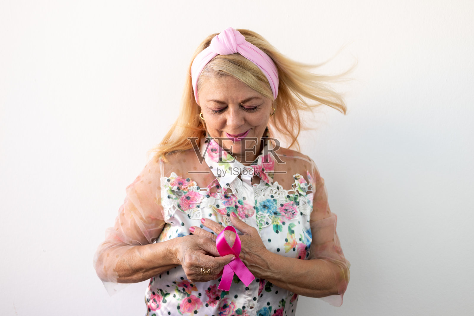 妇女手持象征对抗乳腺癌，金发老妇手持粉红色十月蝴蝶结照片摄影图片