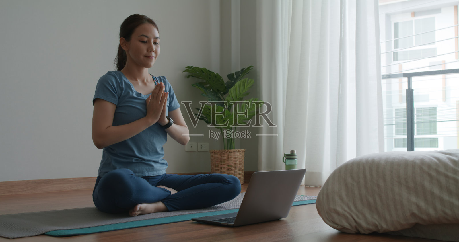 亚洲人运动女人享受学习快乐看现场视频坐在瑜伽垫在舒适的家里地板室内轻松禅宗课。身体平静生活压力放松体式莲花体式在笔记本电脑上自学在线媒体。照片摄影图片