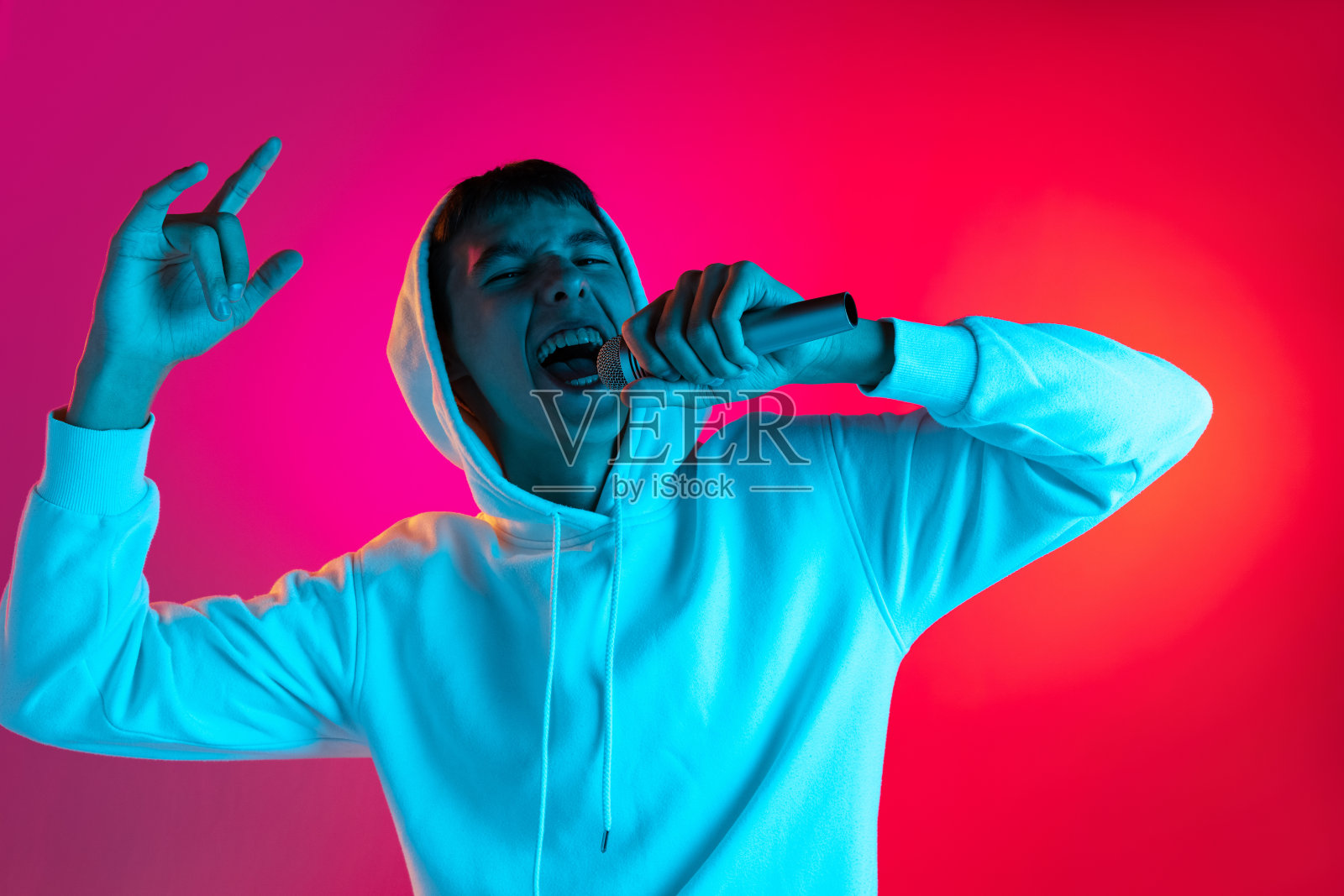 年轻男子的肖像，学生或男孩在休闲服装与麦克风隔离在紫红色工作室背景在霓虹灯。照片摄影图片