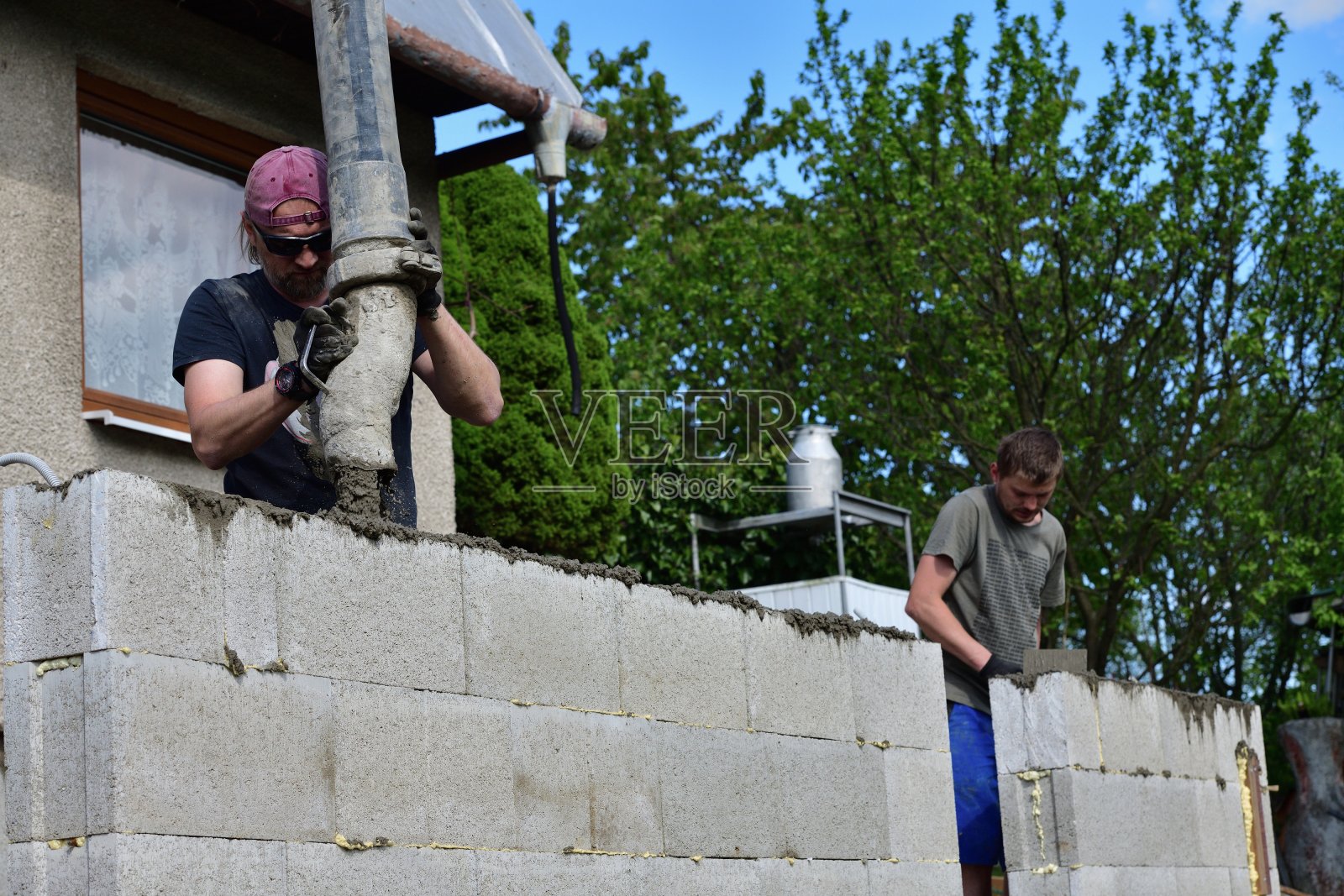在墙壁上浇筑混凝土时，由泥瓦匠和混凝土泵手工制作的组合照片摄影图片