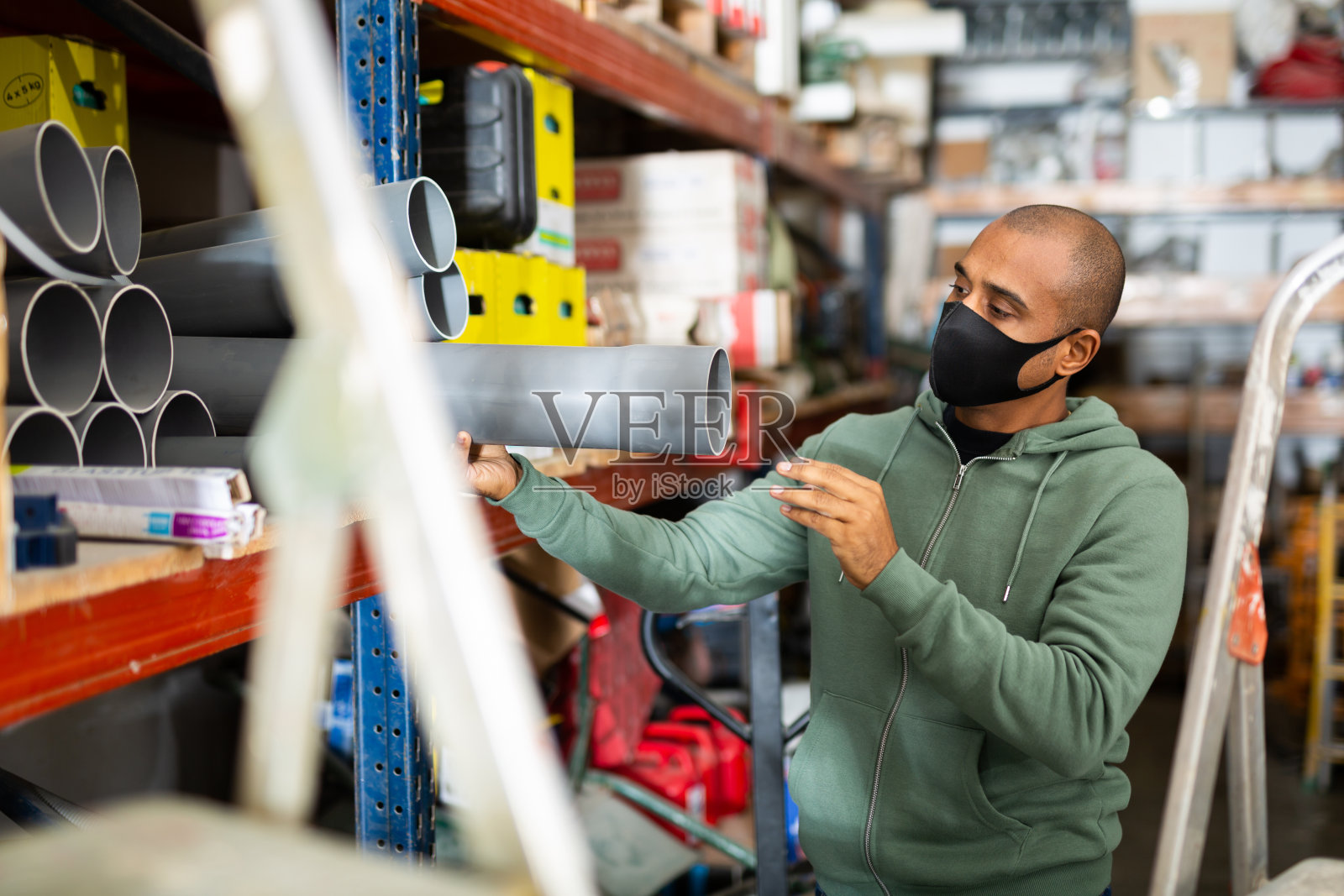 戴着防护面具的工匠在五金店挑选塑料水管照片摄影图片