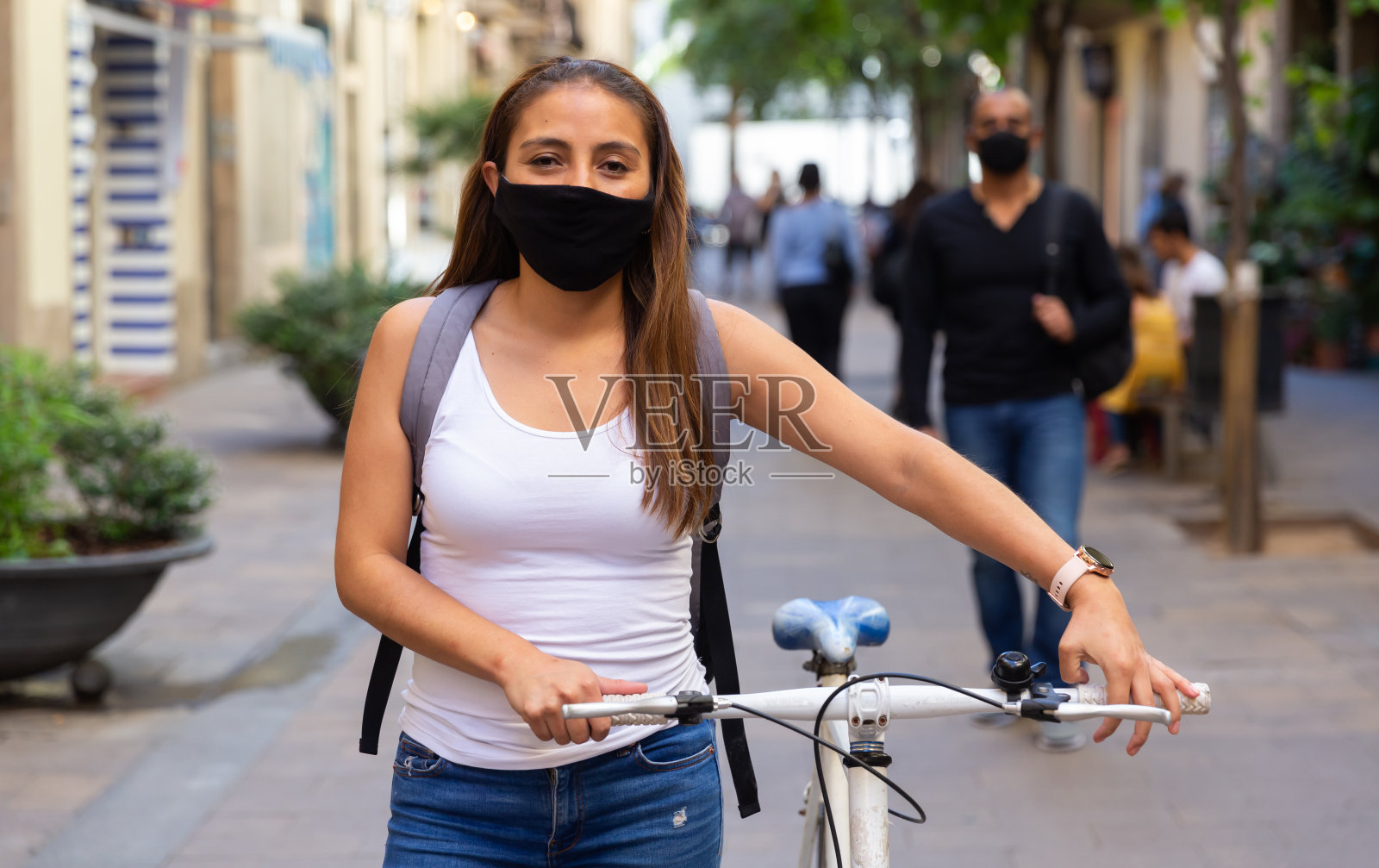 戴着防护面具的女人骑着自行车沿着城市街道走照片摄影图片