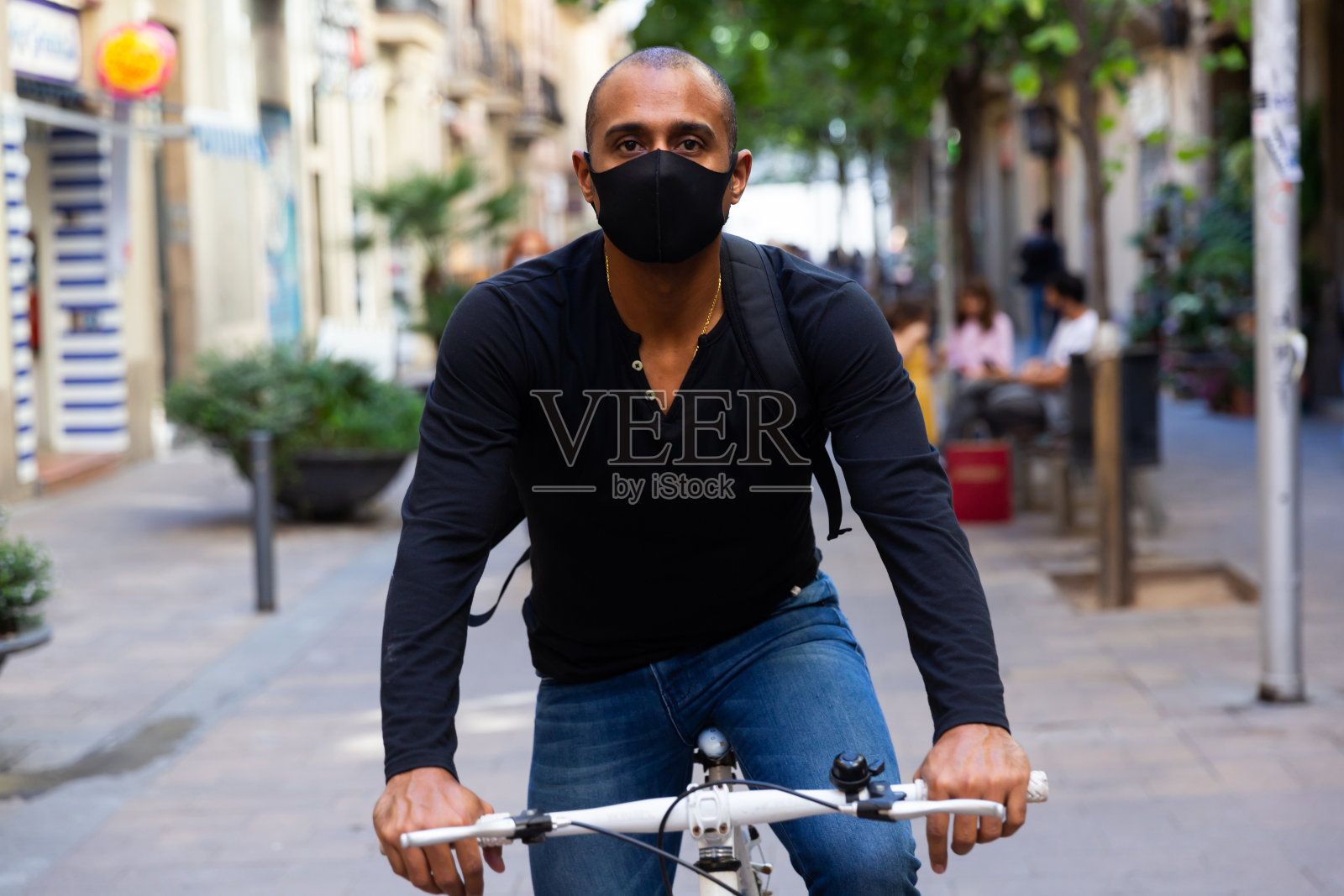 拉丁美洲人戴着防护面具在城市街道上骑自行车照片摄影图片