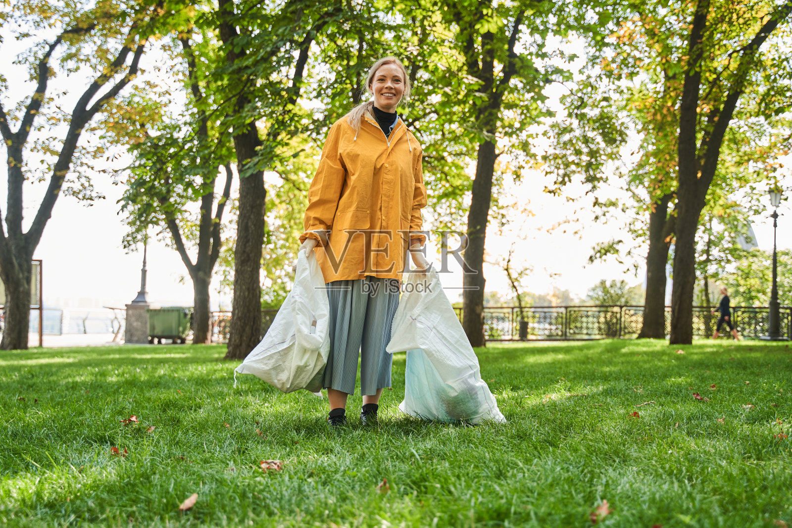 女志愿者拿着两个大垃圾袋，帮助捡垃圾照片摄影图片