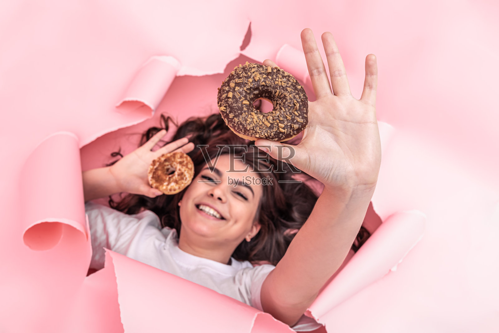 开朗的女孩，粉红色的纸背景上有明亮的甜甜圈。照片摄影图片