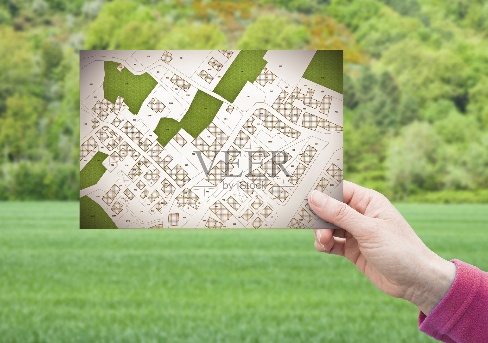土地管理-房地产概念与空地上的绿色住宅区域，可用于建筑施工，手拿一张明信片关于一个虚构的地籍地图照片摄影图片