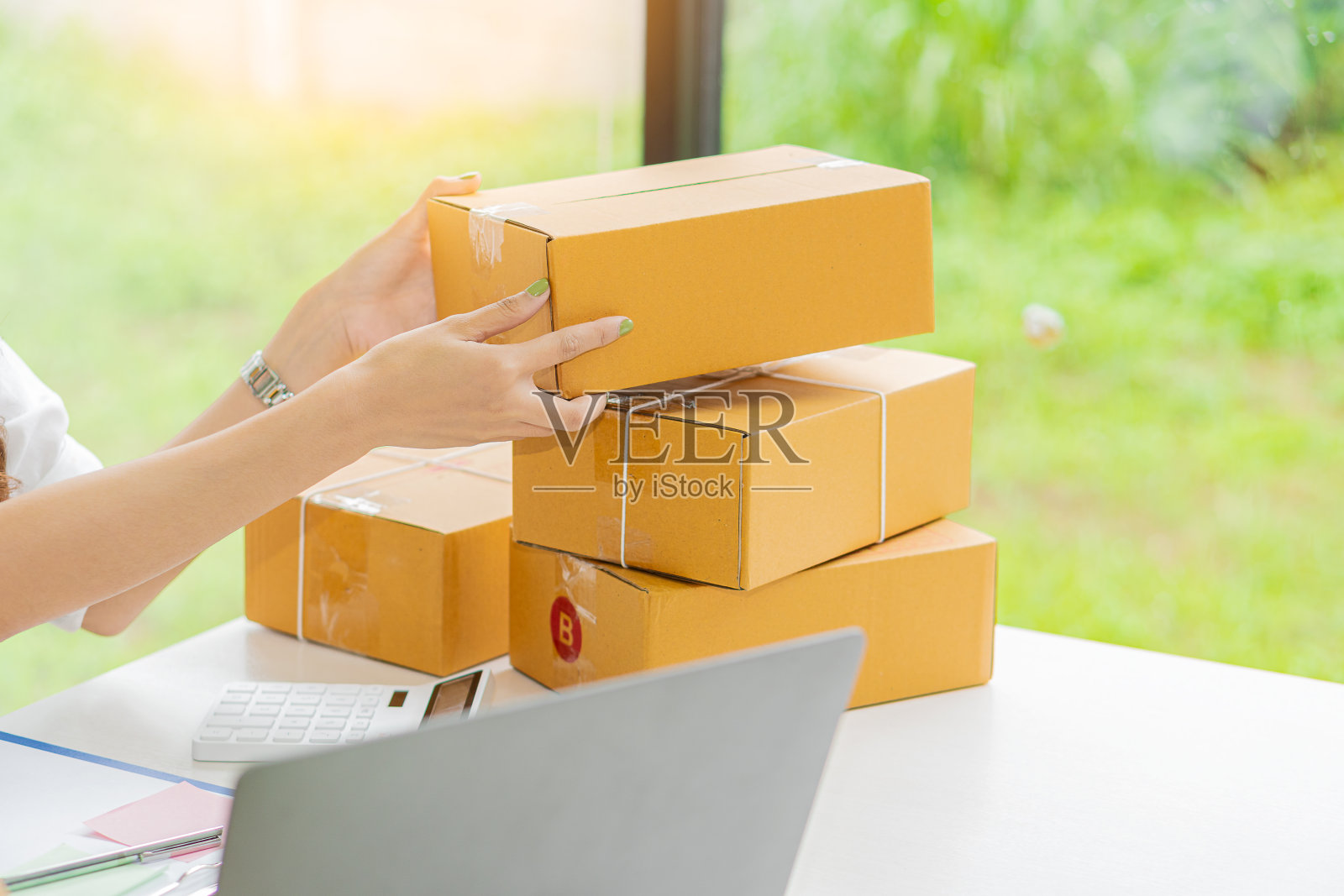 亚洲自由职业女孩中小企业网上购物工作在笔记本电脑，从客户的订单与包裹箱在家庭办公桌-中小企业网上业务的想法和送货。照片摄影图片