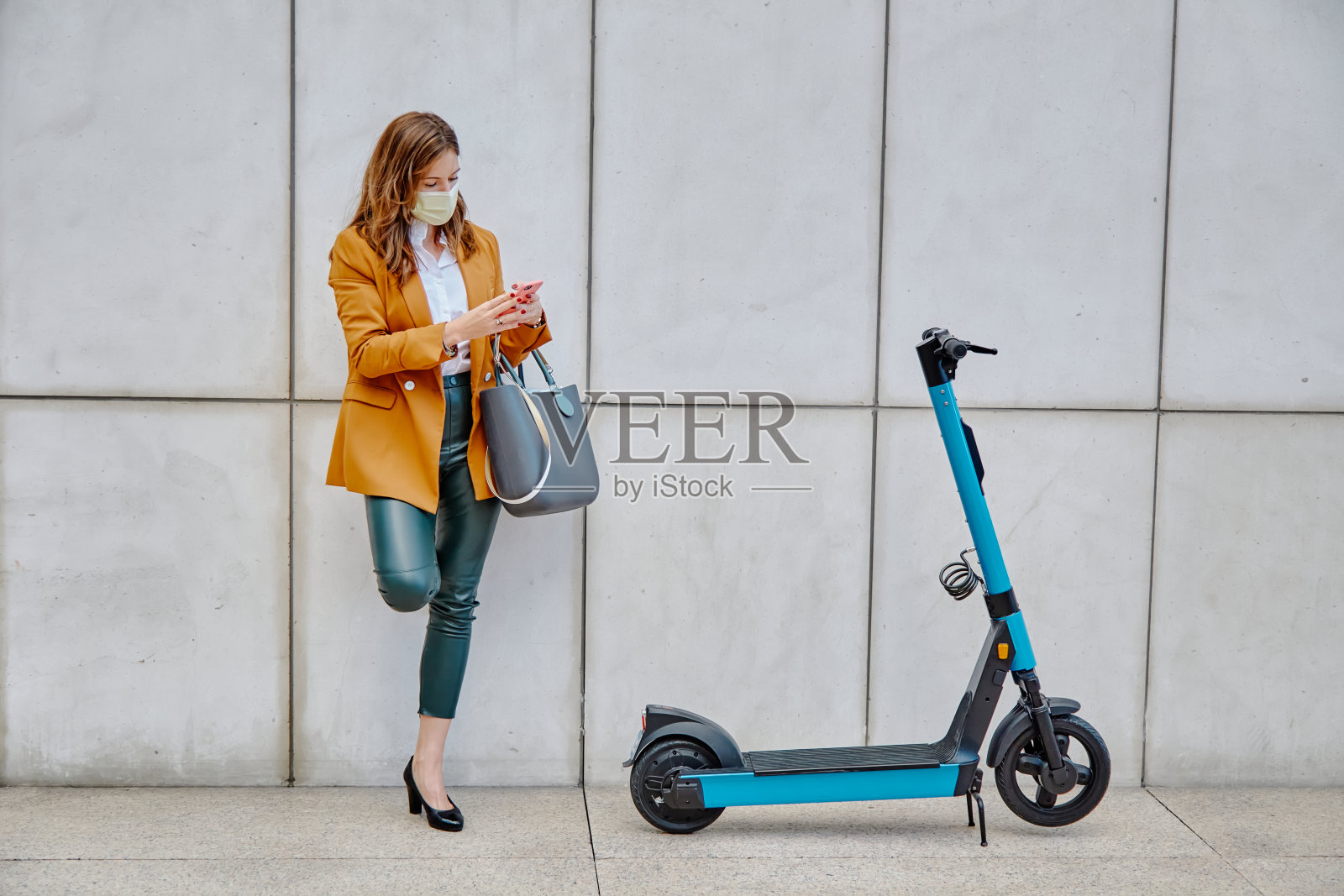 年轻女子在城市里租用电动滑板车-使用智能手机租用电动滑板车的女子照片摄影图片