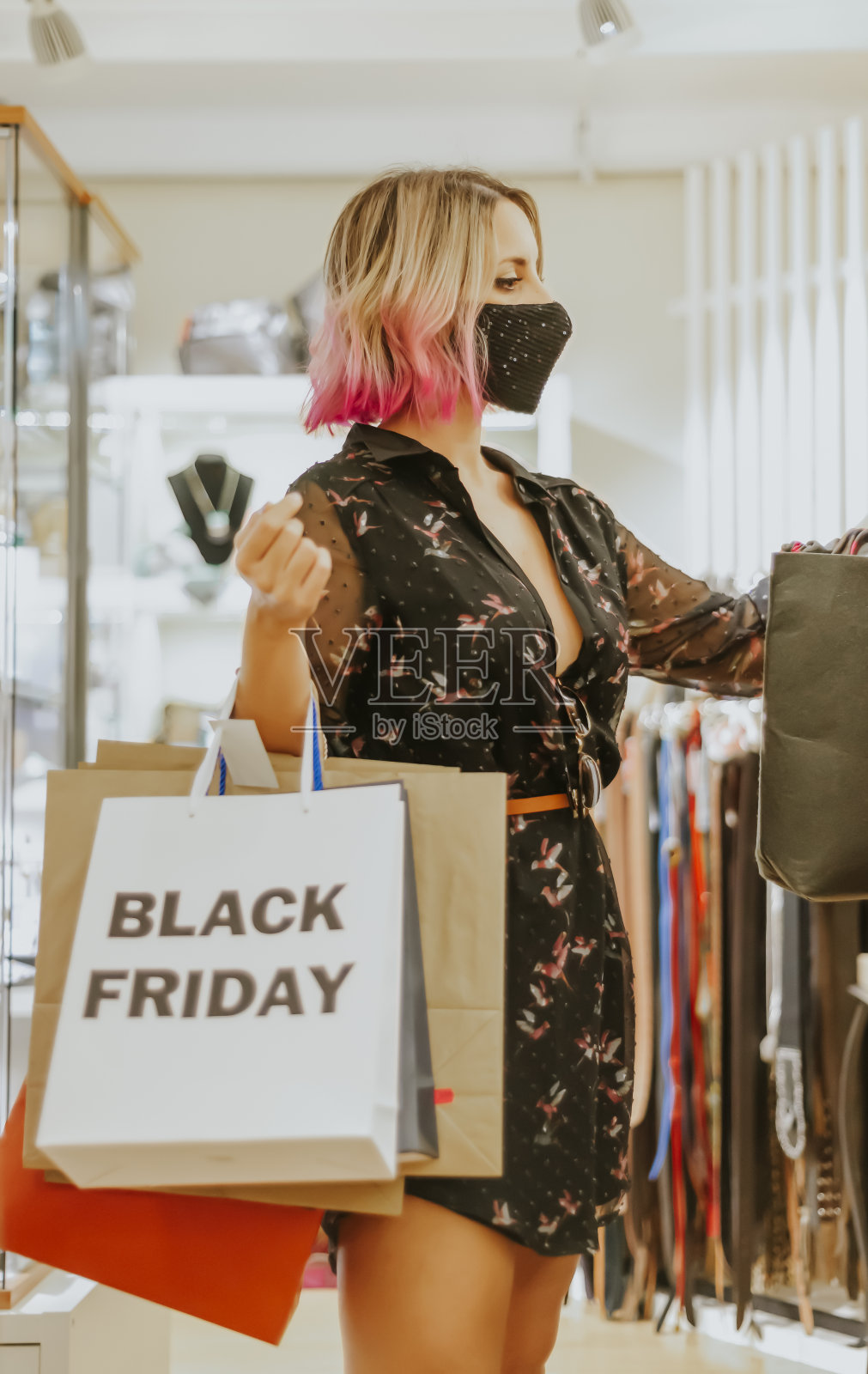 一个年轻的金发碧眼的粉红色头发，戴着一个防护面具，在一个有购物袋的服装店。照片摄影图片