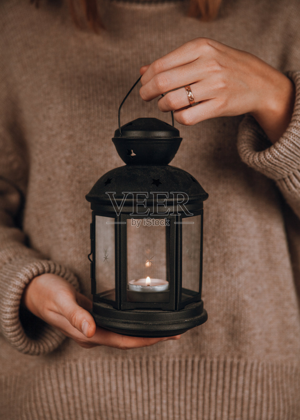 女孩在舒适的米色毛衣手握黑色复古灯与燃烧的蜡烛。照片摄影图片