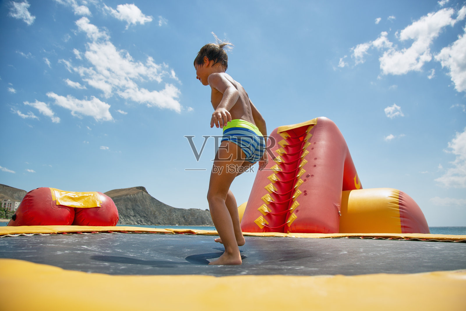 男孩在阳光明媚的日子在海上玩水上蹦床照片摄影图片