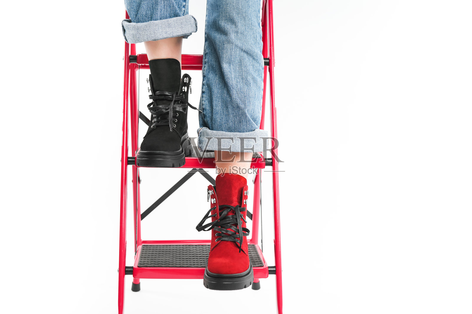 女孩穿着时髦的黑色和红色皮靴在白色背景下的工作室楼梯上摆姿势。照片摄影图片