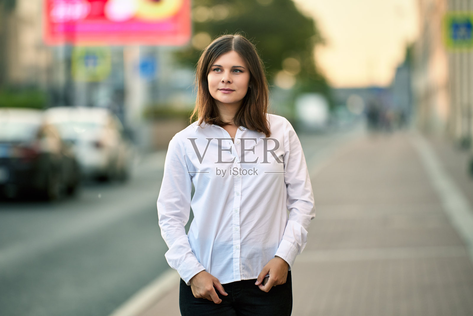 一个穿着衬衫的白人年轻女子在夏日的车流旁站着。照片摄影图片