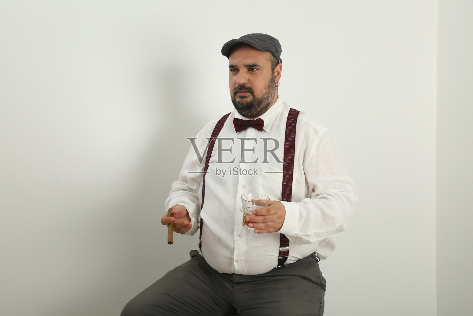 穿着亚麻衬衫和衣架，抽着雪茄和威士忌，用手势说着什么的年轻男人照片摄影图片