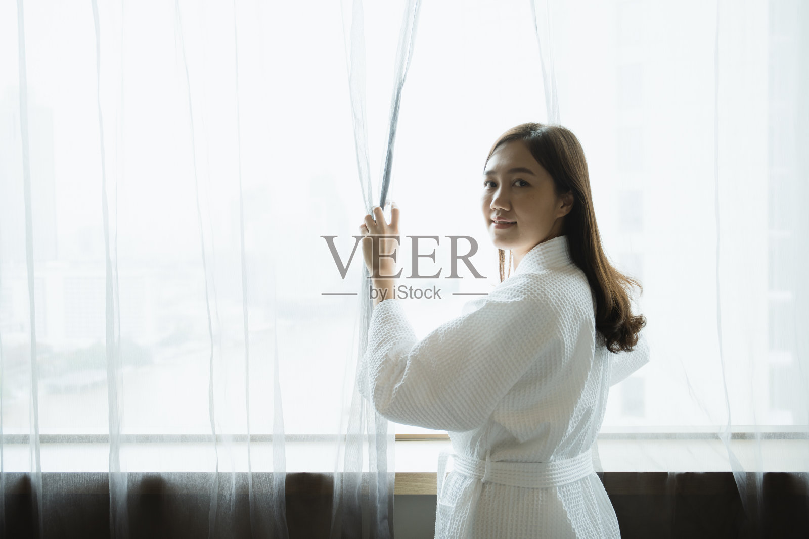 女人拉开窗帘。照片摄影图片