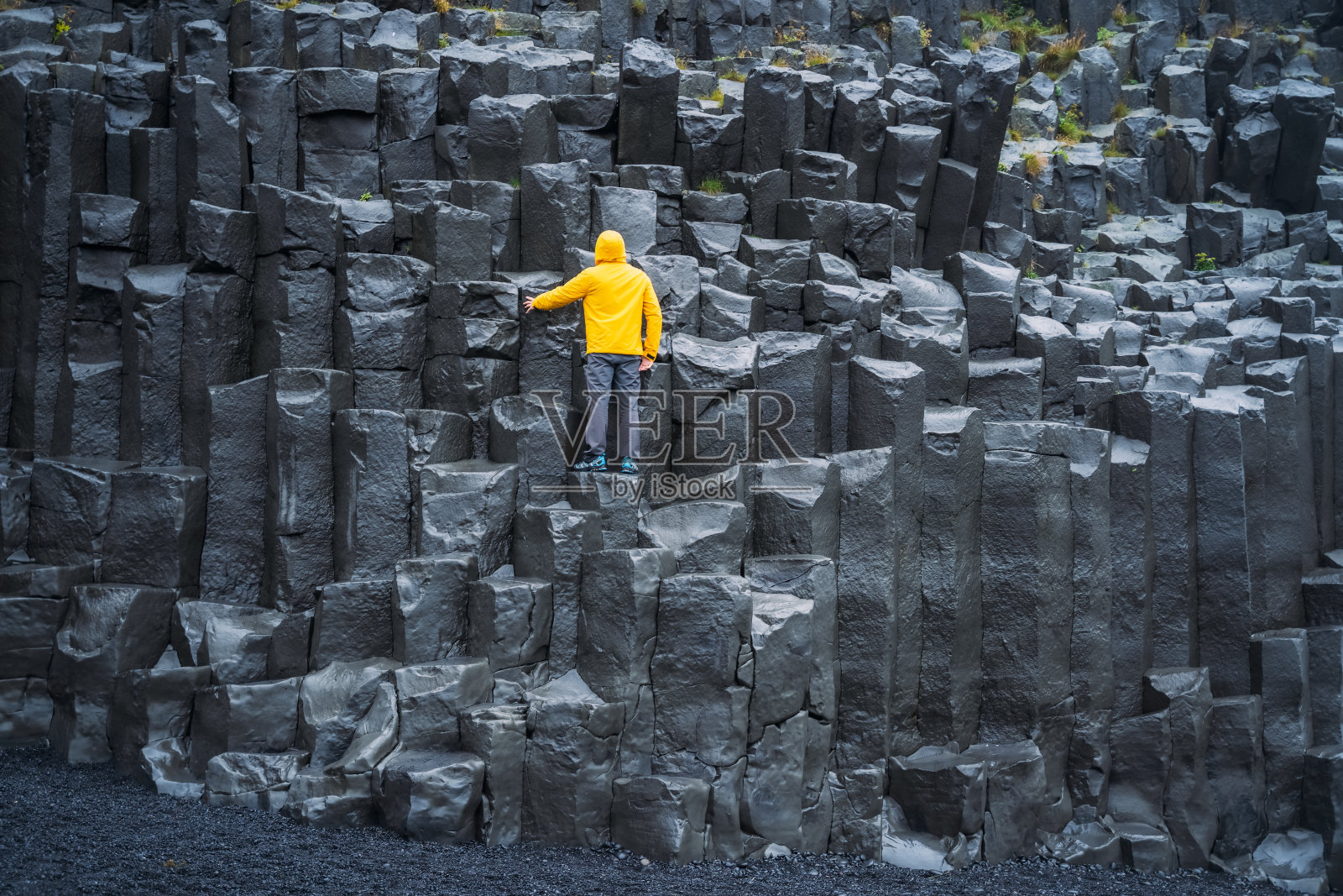 一名身穿黄色外套的男子抬头望着冰岛雷尼斯菲加拉海滩的雷尼斯德拉加尔玄武岩柱照片摄影图片
