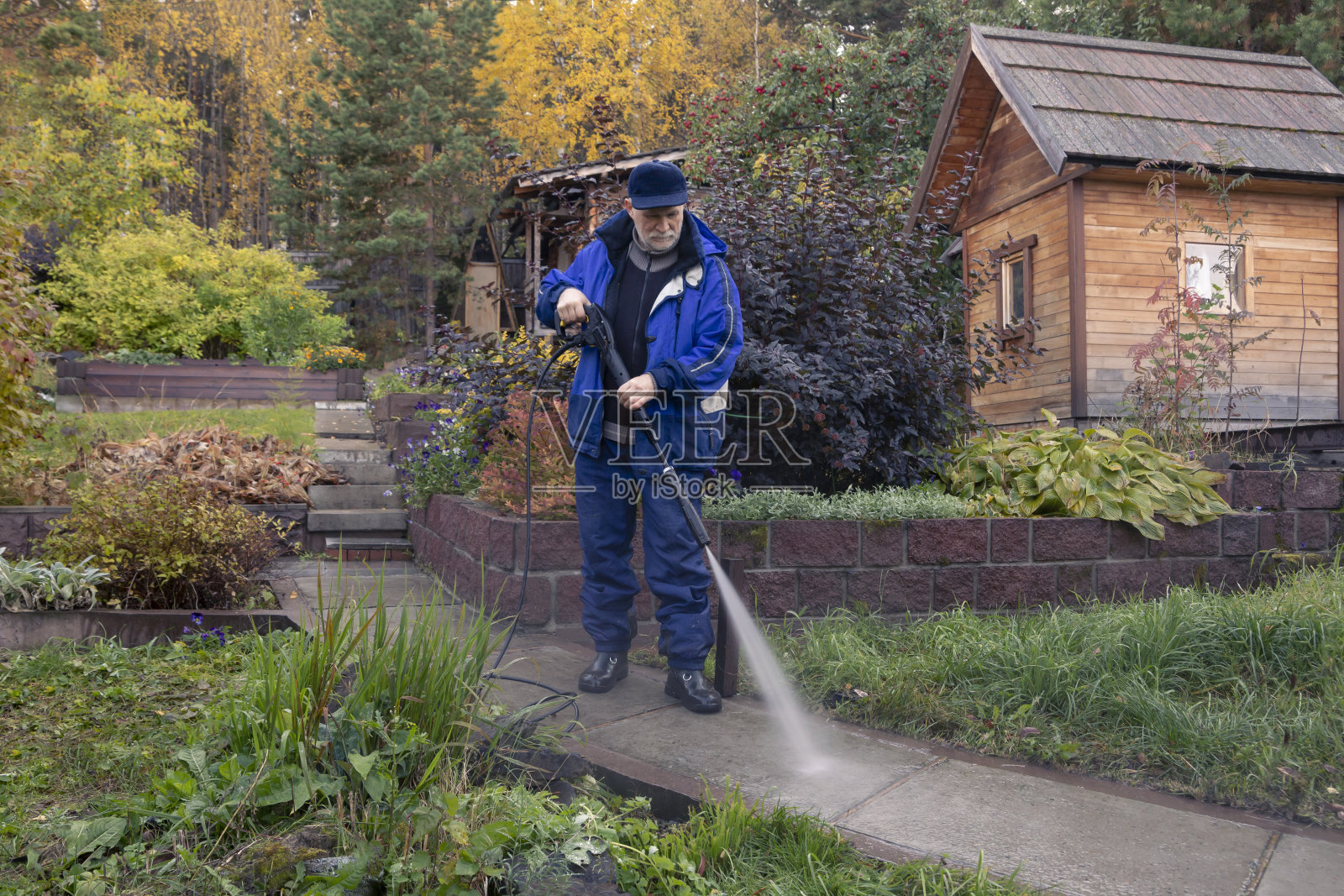 一名男子用高压清洗机清洗花园小径。秋天在花园里工作。照片摄影图片