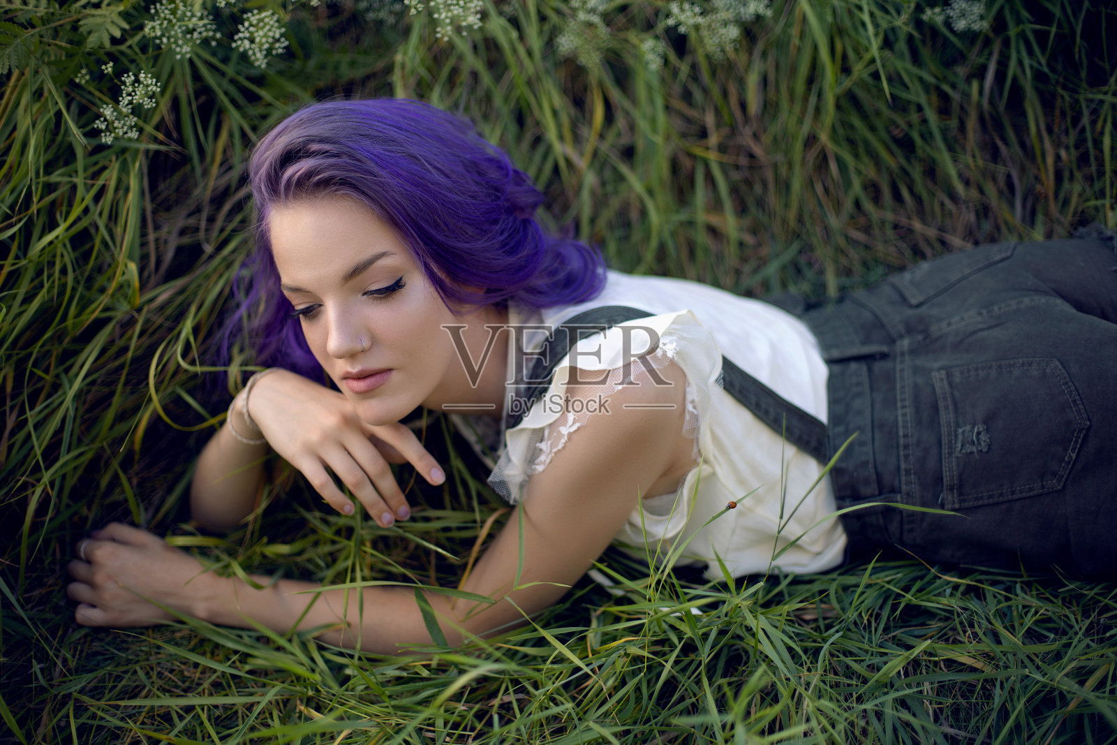 草地上躺着一个紫色头发鼻子上戴着耳环的少女的画像照片摄影图片