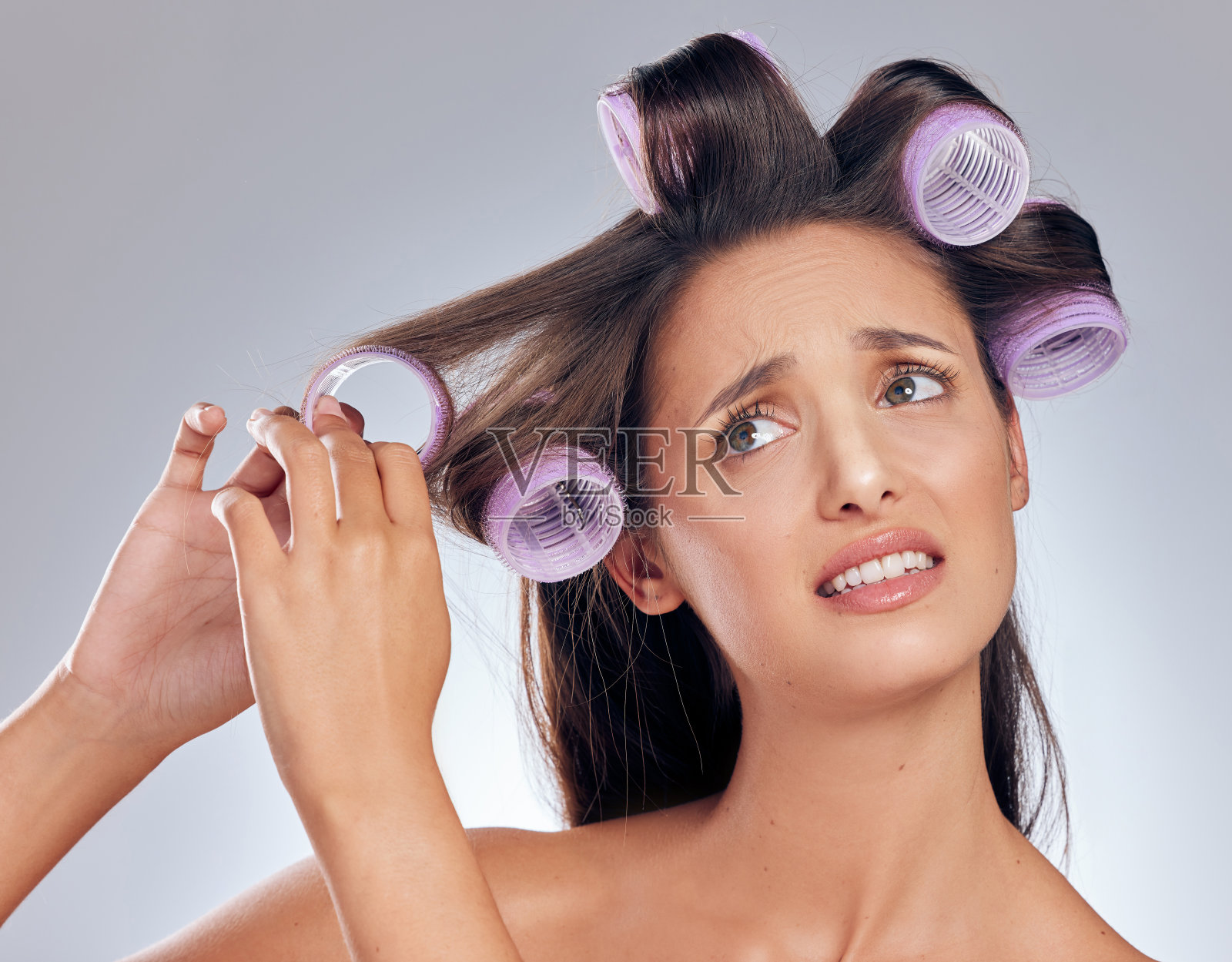 一名年轻女子站在摄影棚里，压力很大，她试图把卷发器卷起来照片摄影图片