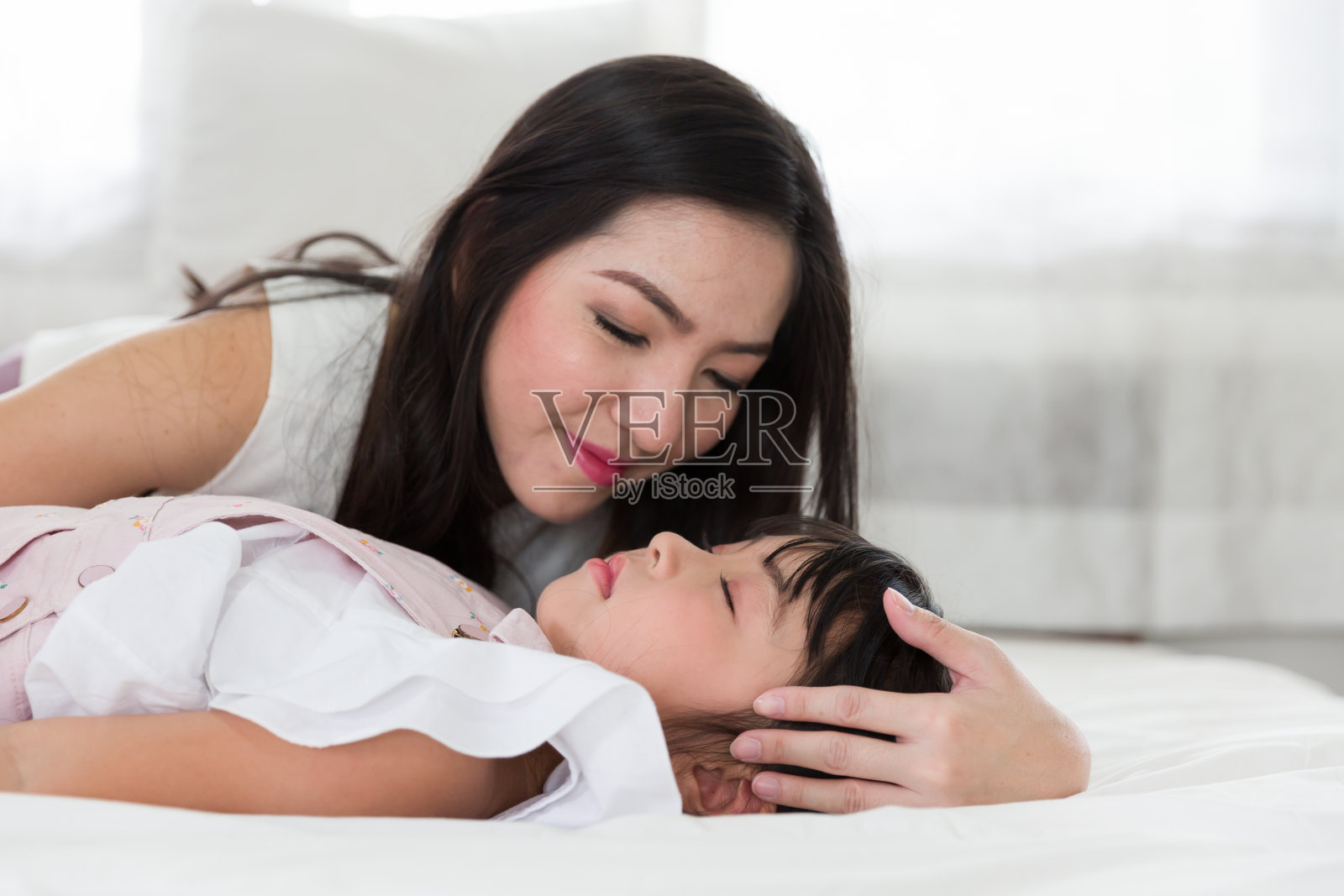 亚洲年轻的母亲小心翼翼地把女儿放在家里的床上睡觉照片摄影图片