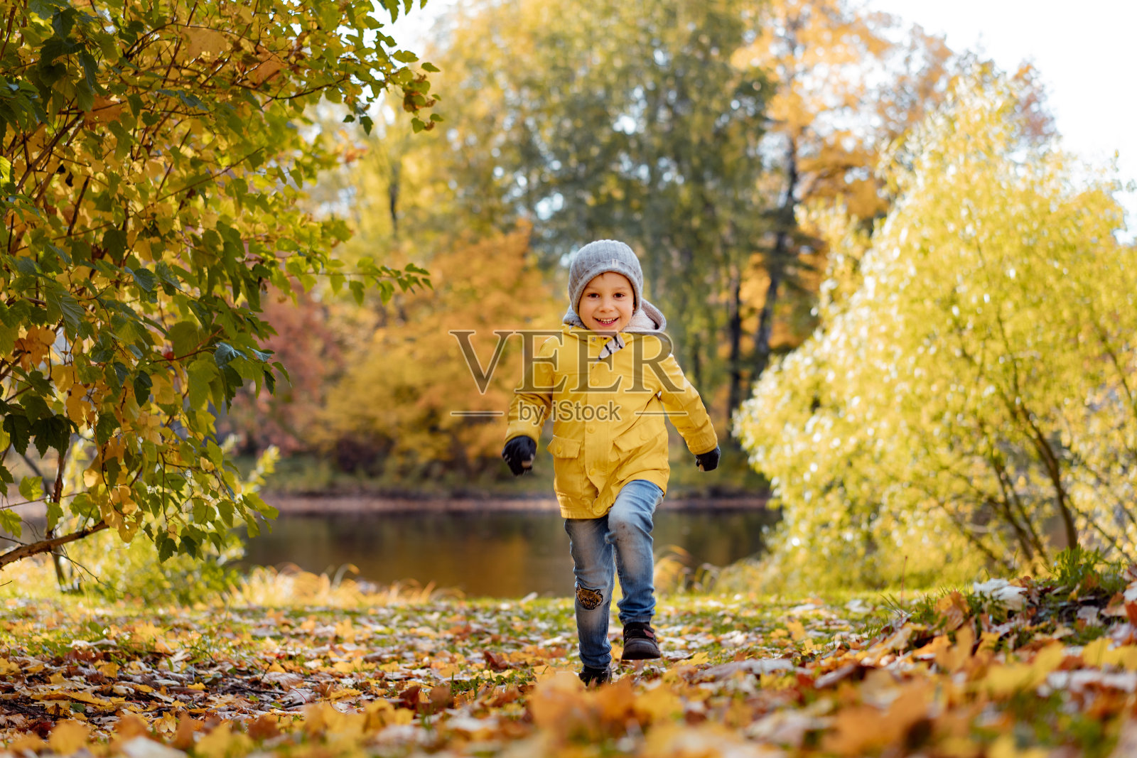 在十月阳光明媚的日子里，一个穿着黄色夹克的快乐小男孩在俄罗斯圣彼得堡的秋天中央公园跑步照片摄影图片