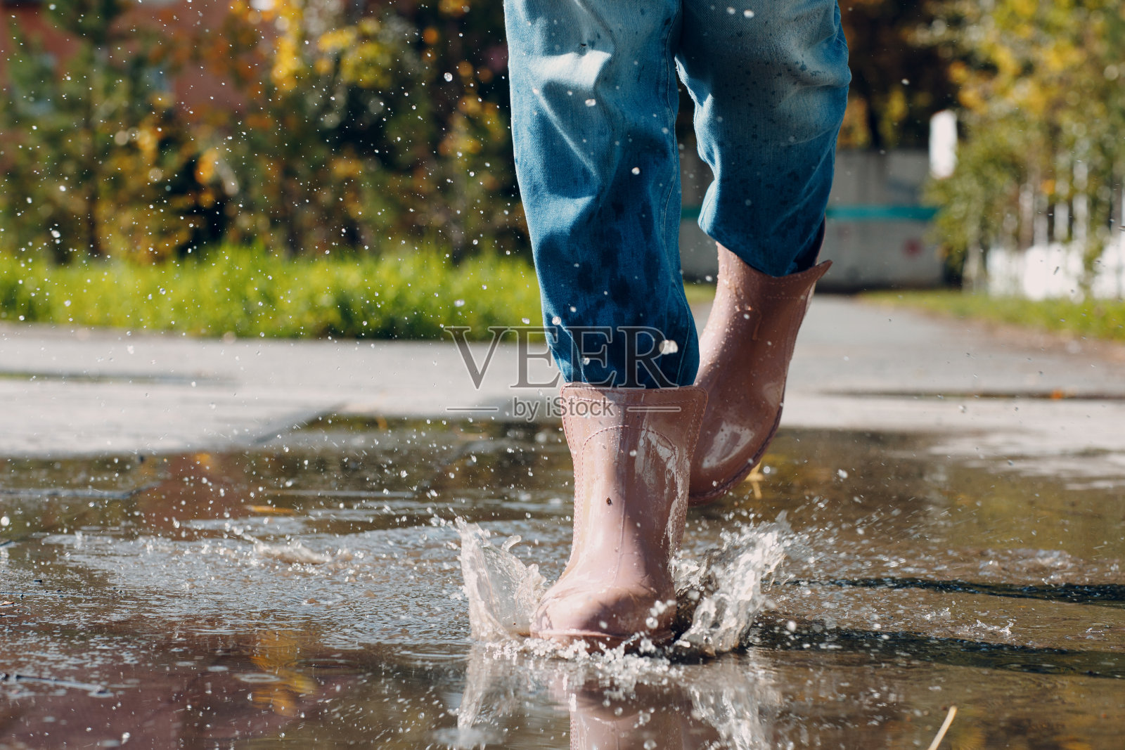 穿着雨靴的女子在秋雨中走着、跑着、跳进水坑里，水花四溅，水花四溅照片摄影图片