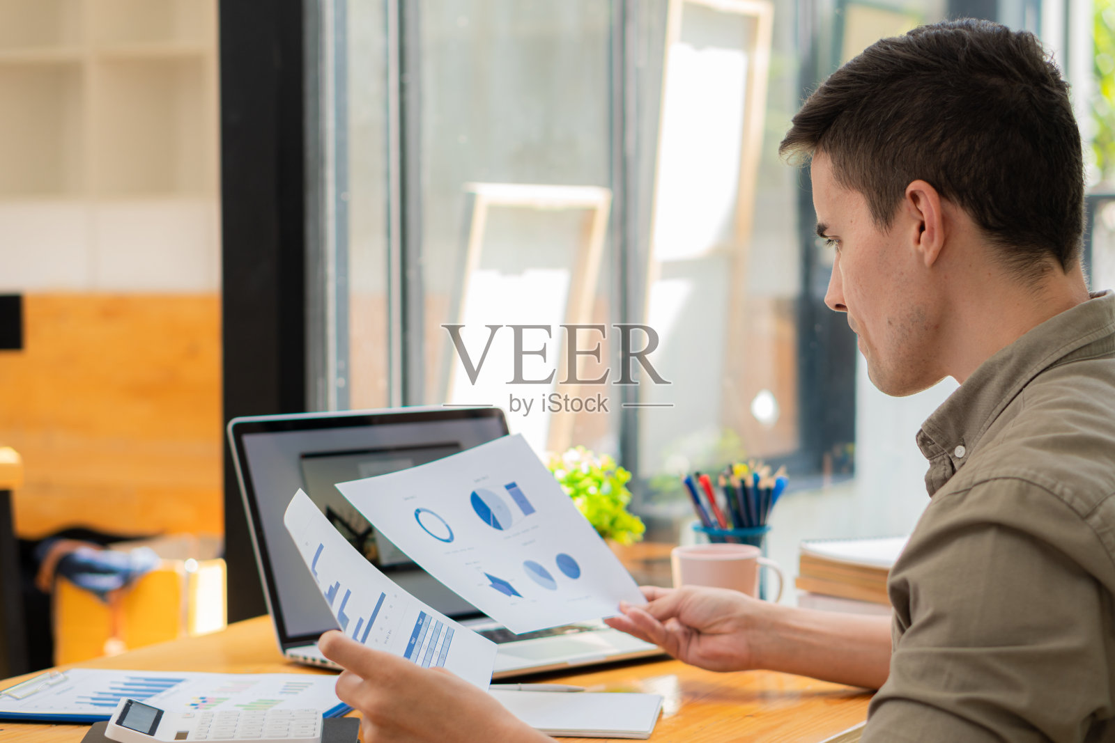 年轻男商人用笔记本电脑和计算器分析财务报告图表数据。财务会计和投资概念照片摄影图片