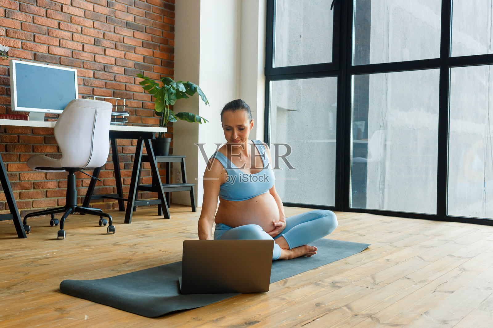 一位孕妇坐在蓝色瑜伽垫上，一边用笔记本电脑工作照片摄影图片