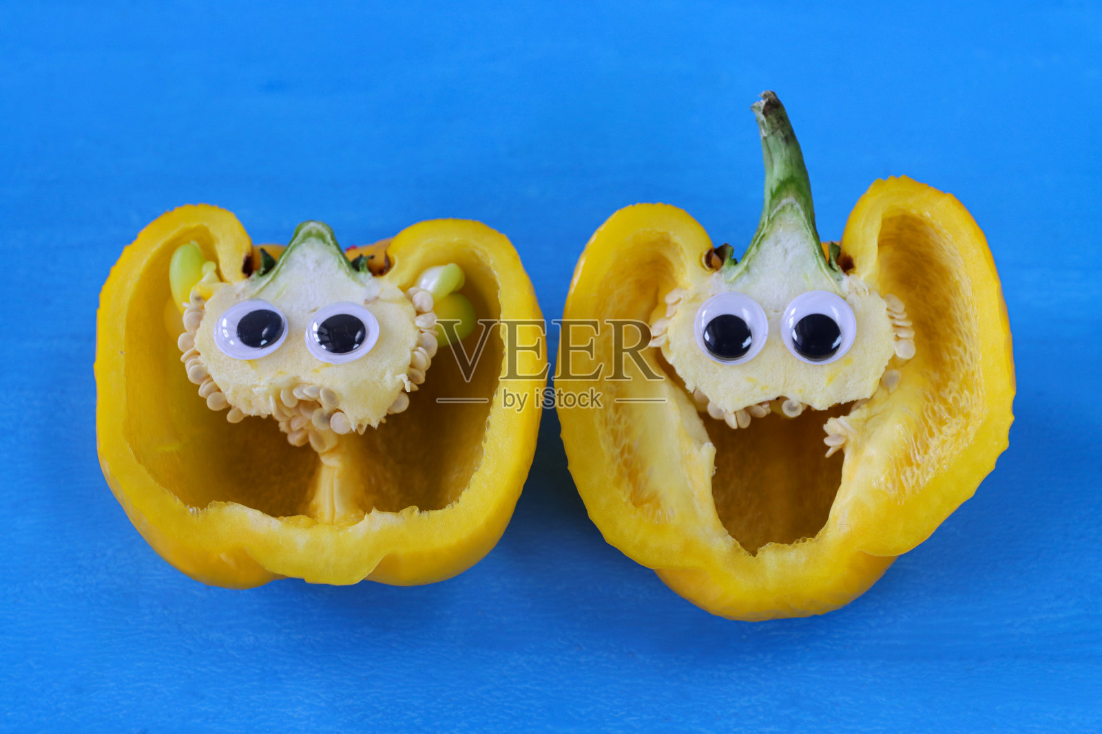 黄色甜椒切成两半，显示果皮(子房壁)、种子、胎盘、隔和室室、卡通脸、幽默概念、蓝色背景照片摄影图片