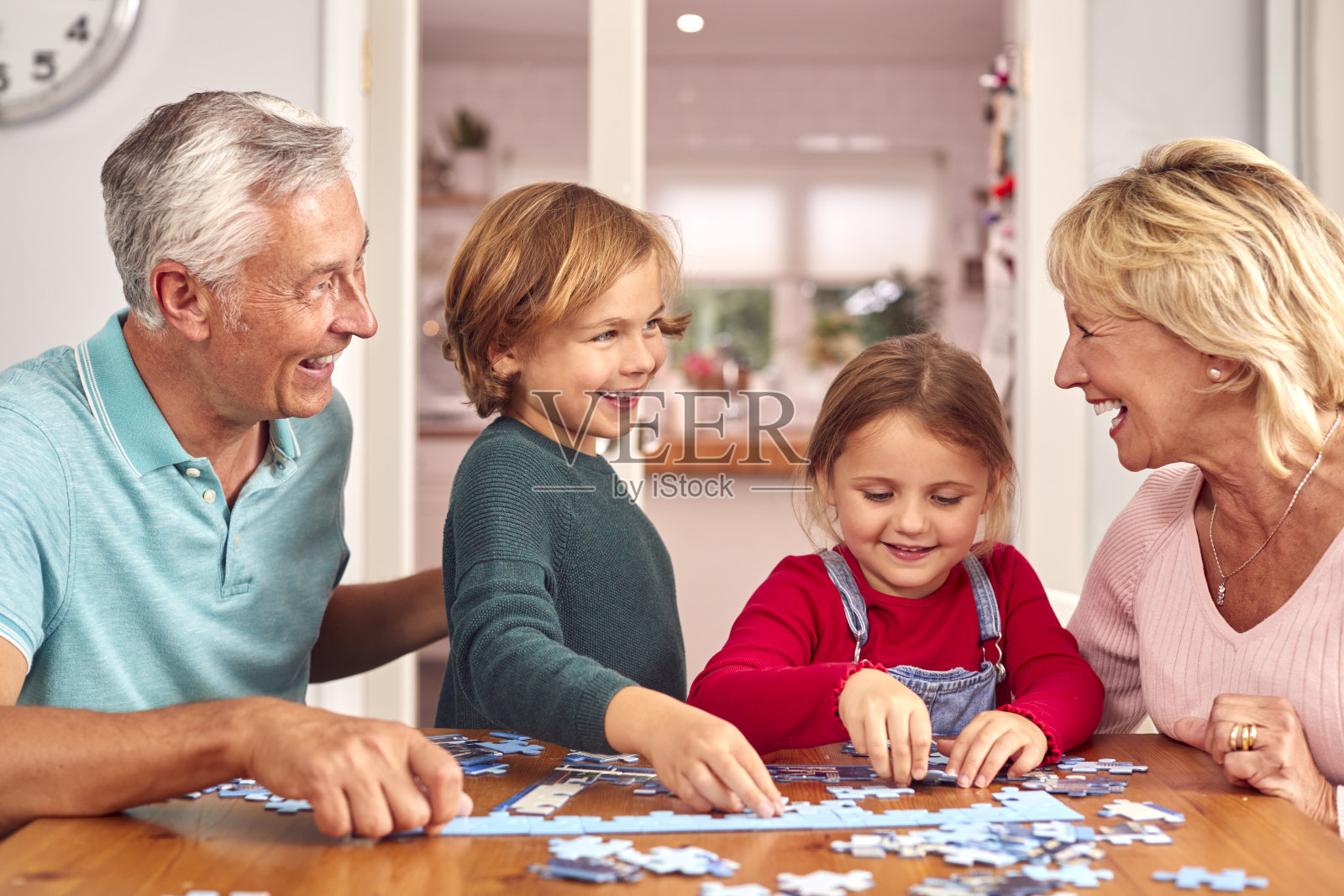 孙辈和祖父母围坐在家里的桌子旁一起玩拼图游戏照片摄影图片