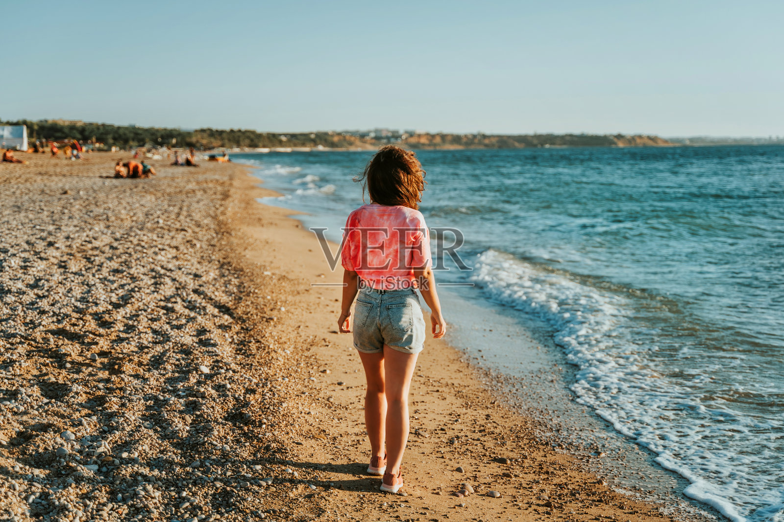 一位年轻美丽的女子沿着海滩散步，欣赏日落时的海景照片摄影图片