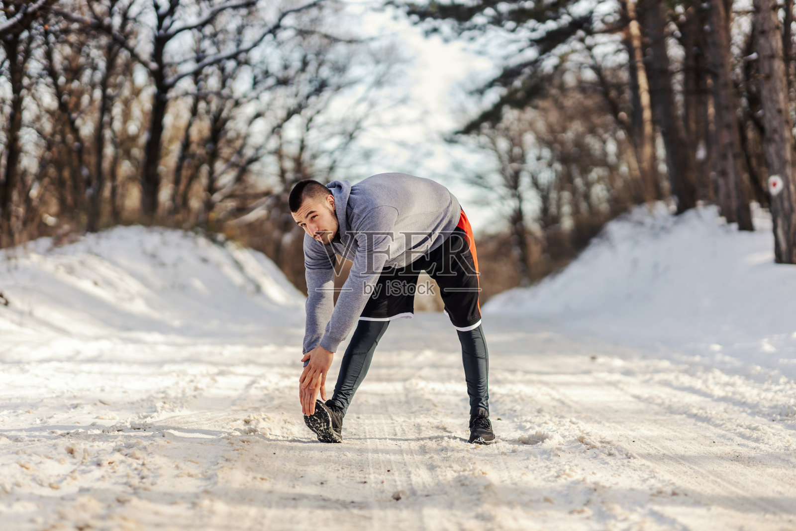 健美的运动员站在雪道上做热身和伸展运动。冬季健身，身体柔韧，生活健康照片摄影图片