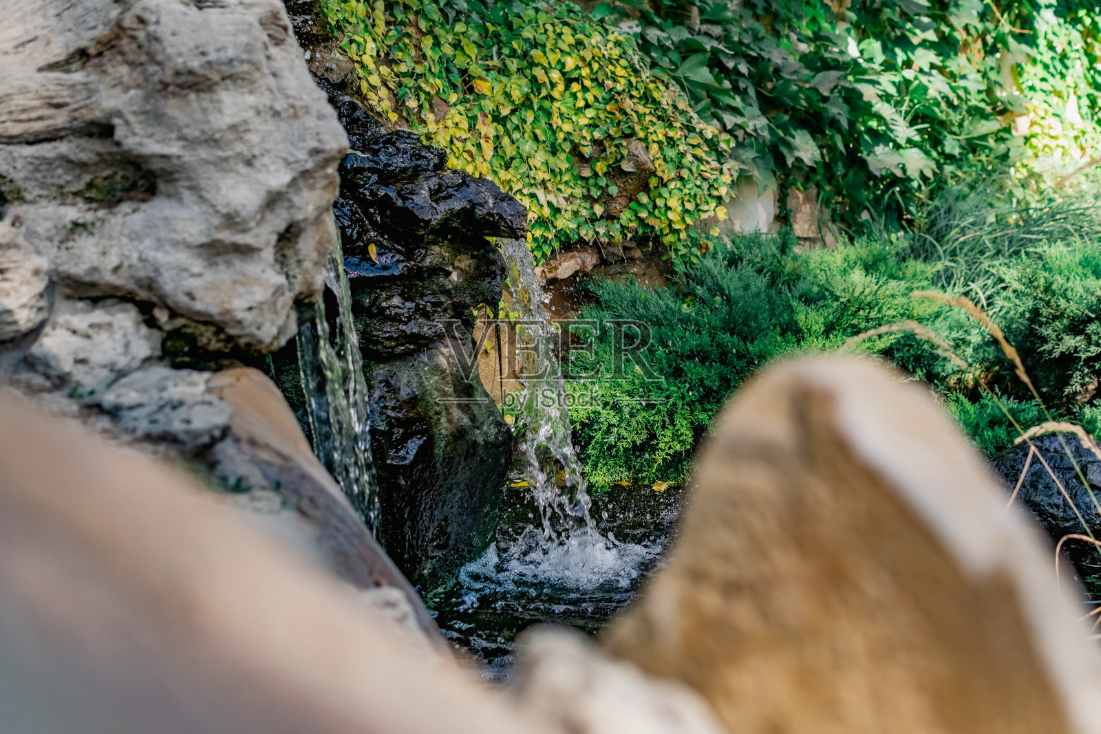 一个美丽的人工瀑布在一个平静的池塘，装饰着有趣的植物和不寻常的石头和装饰品，在公园里散步在新鲜的空气照片摄影图片