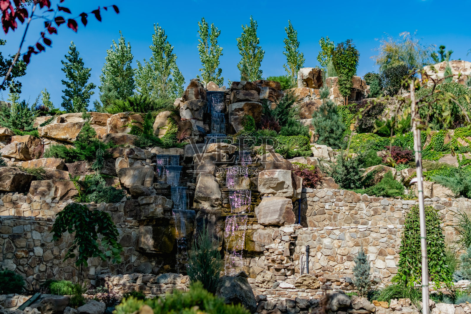 一个美丽的人工瀑布在一个平静的池塘，装饰着有趣的植物和不寻常的石头和装饰品，在公园里散步在新鲜的空气照片摄影图片