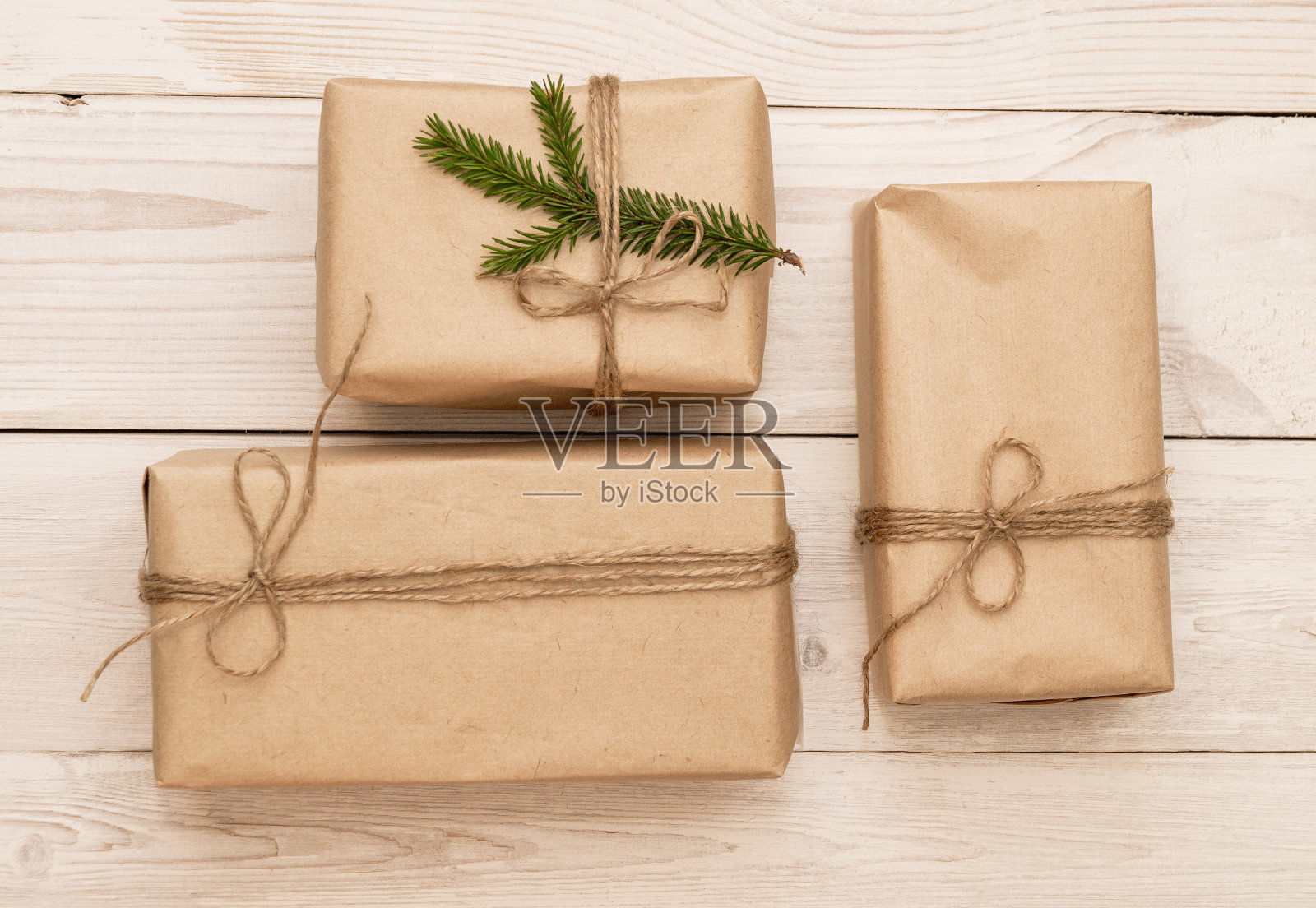白色木制背景上的现代手工圣诞礼物。棕色牛皮纸，黄麻线，亚麻绳，杉木树枝，礼物装饰品。俯视图，DIY概念照片摄影图片
